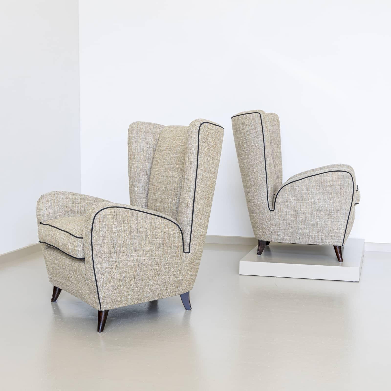 Pair of wingback armchairs in the style of Paolo Buffa with high backrests and rounded, deep-cutting armrests. The armchairs stand on dark stained conical feet. The armchairs are newly upholstered in a beige and white mottled fabric and decoratively