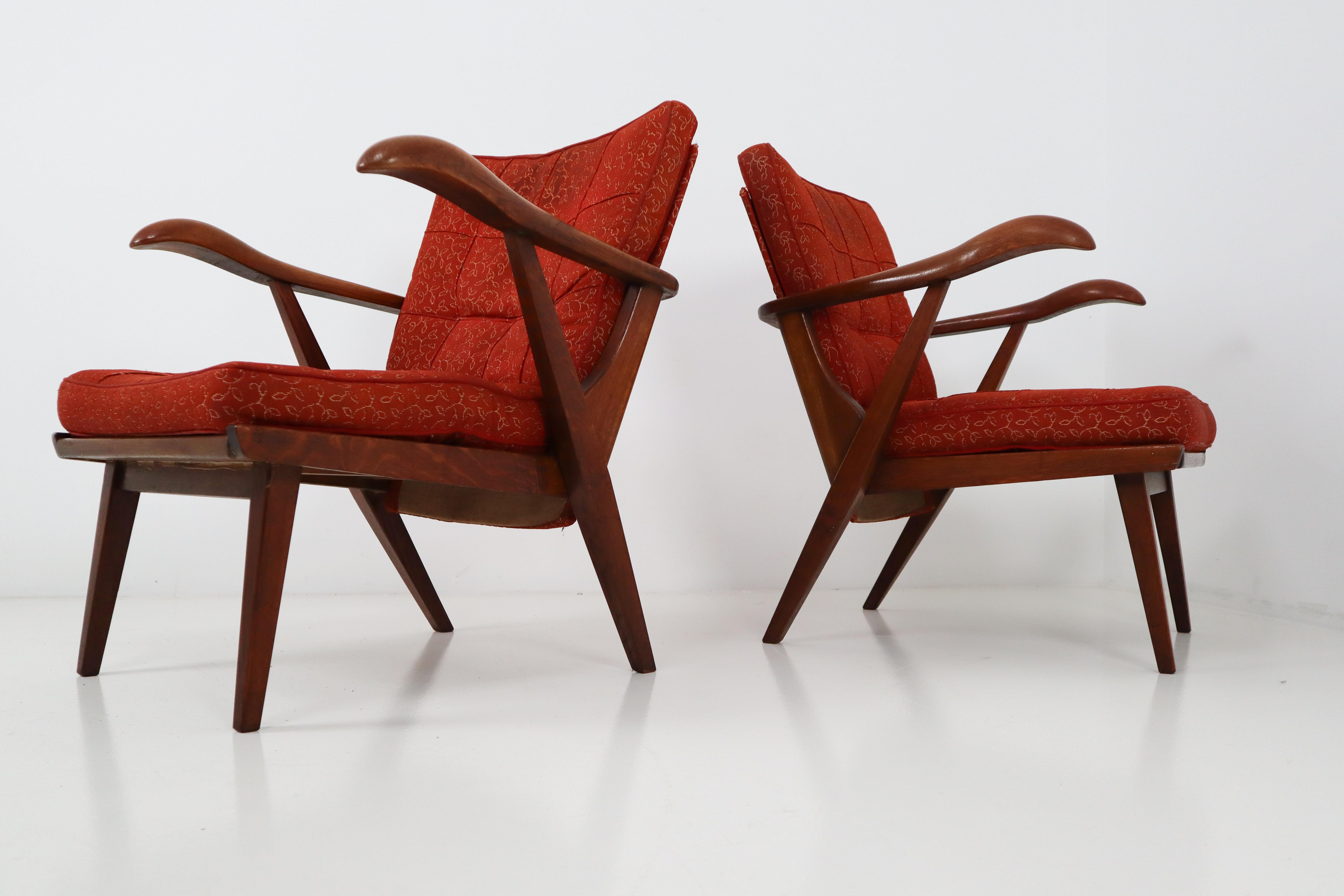 Set of two lounge chairs, in patinated solid oak and red fabric, Czech Republic, 1950s. The grain of the stained wood is nicely visible, especially on the wide sculpted armrests. Amazing original patina. These chairs are upholstered in original red