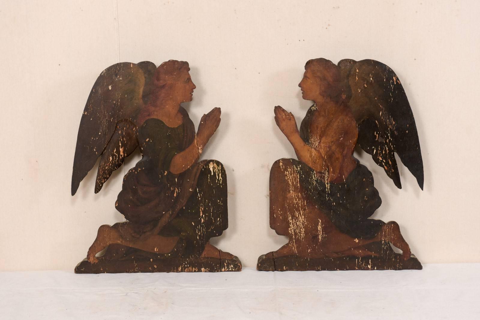 A pair of Italian 19th century painted wood angel plaques. This pair of antique Italian plaques, perhaps originally used to decorate a chapel, feature a pair of facing winged angels, head's straight, bent on one knee, with palms together in praying