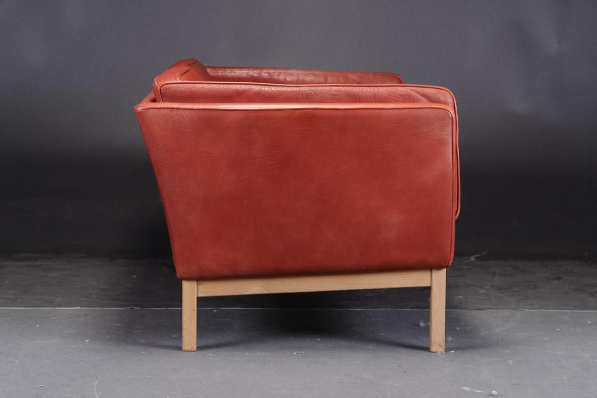 Pair of Danish modern loveseats by Vatne Møbler. Two-seat sofas, model 'Forum', loose cushions upholstered in patinated, deep red buffalo leather, deep-stitched back cushions, legs and solid ash frame. L. 145 cm. Sh. 43 cm. Slight traces of wear