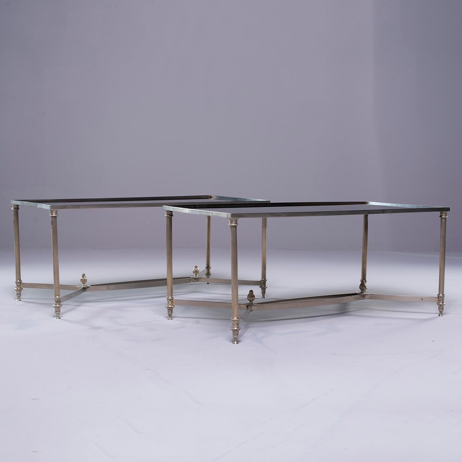 Pair of French circa 1940s pair of cocktail tables in the style of Maison Baguès feature silver tone metal frames with reeded legs and stretchers accented with finials. Inset black glass table tops. Sold and priced as a pair. Unknown maker.