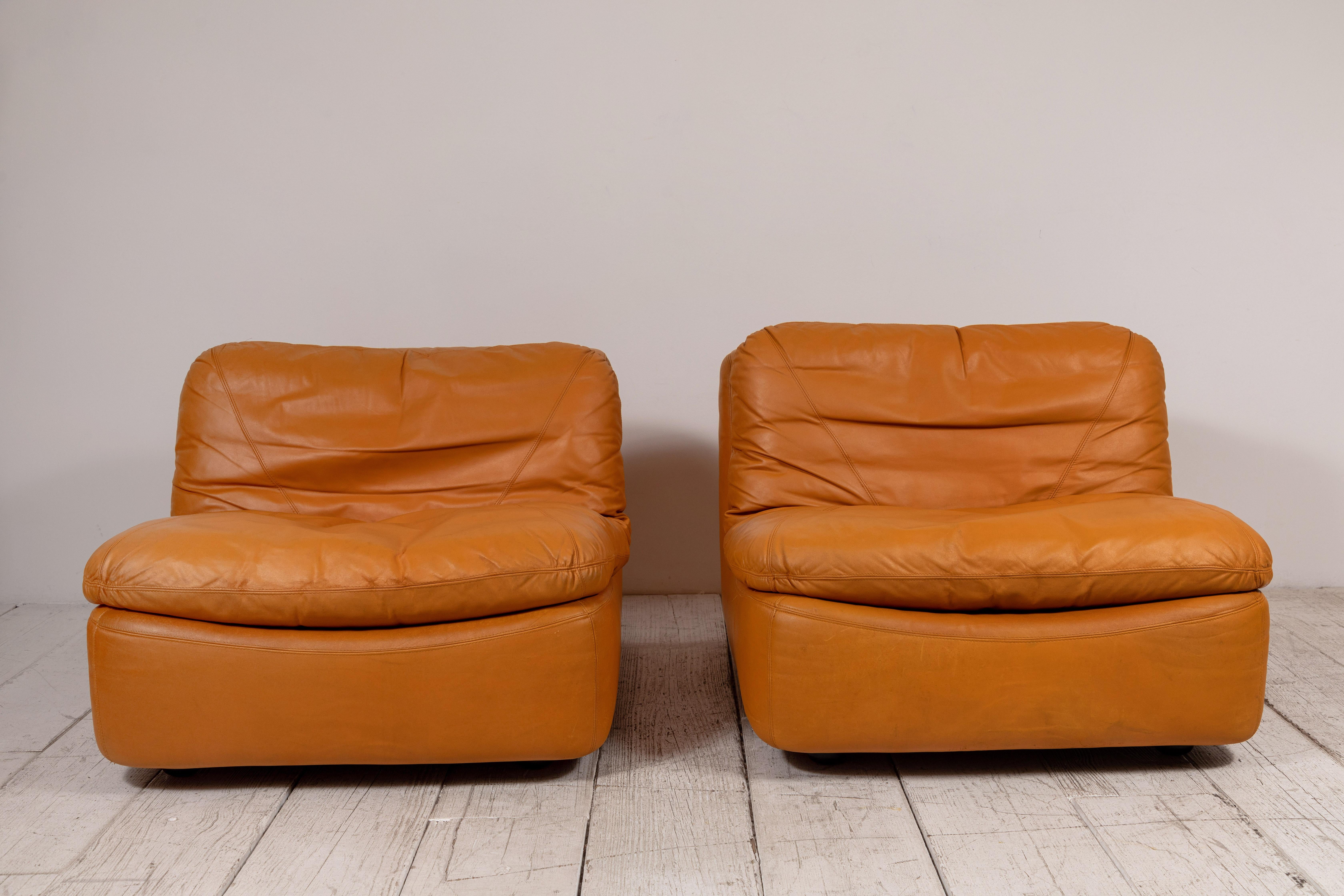 This pair of low relaxed slouchy lounge chairs has boxed frame with comfy seat cushions that rest on top of the frame structure. The armless low chairs offer unique leather stitching. The design is very rare.
 