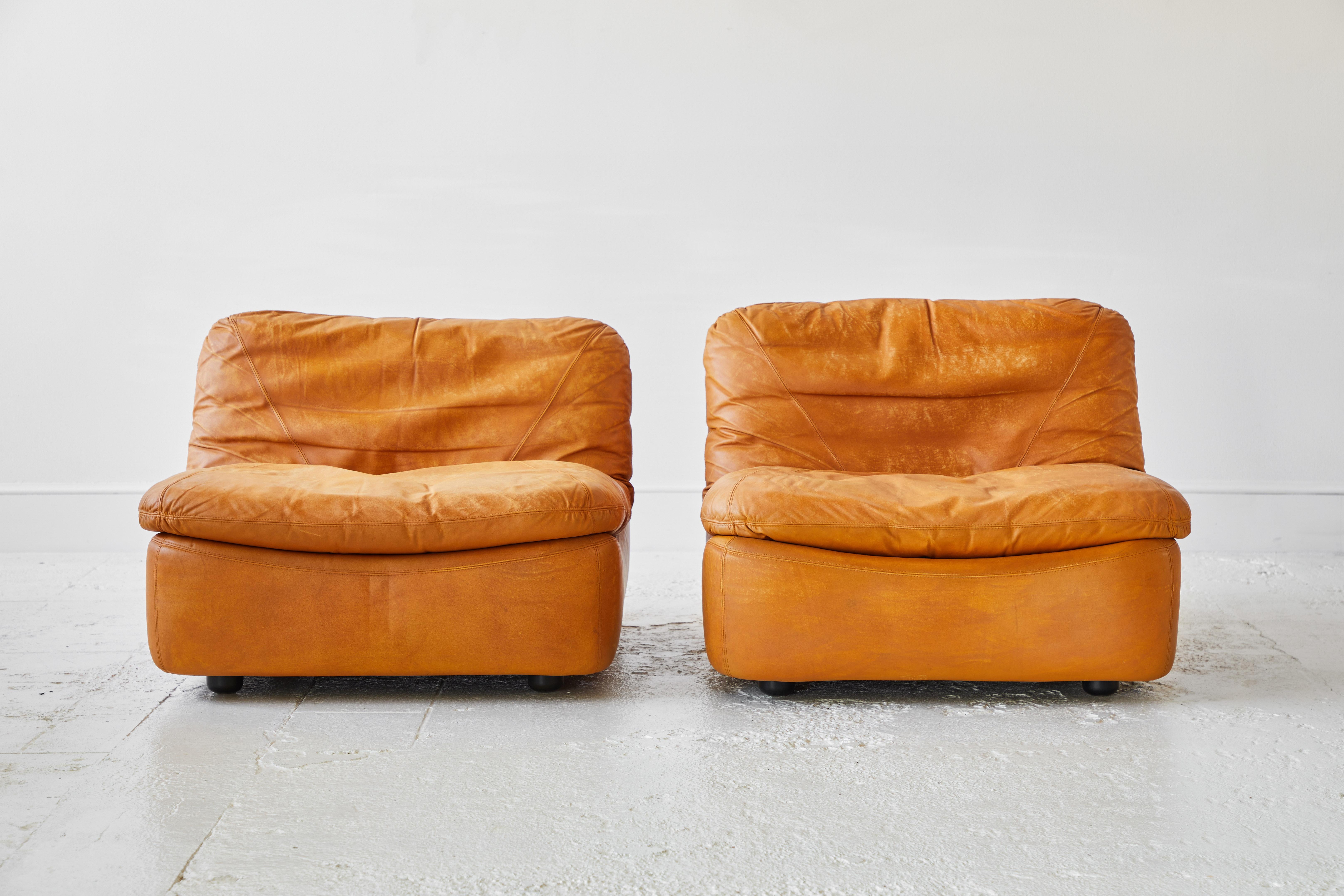 This pair of low relaxed slouchy lounge chairs has boxed frame with comfy seat cushions that rest on top of the frame structure. The armless low chairs offer unique leather stitching. The design is very rare.