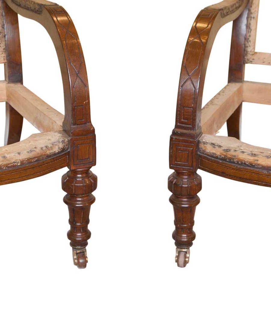 Pair of low oak 19th century Gillows style armchairs.
A pair of good sized armchairs circa 1890, the crest and the arms with carved geometric design, turned fluted baluster legs with brass castors.

Measures: Seat depth 25