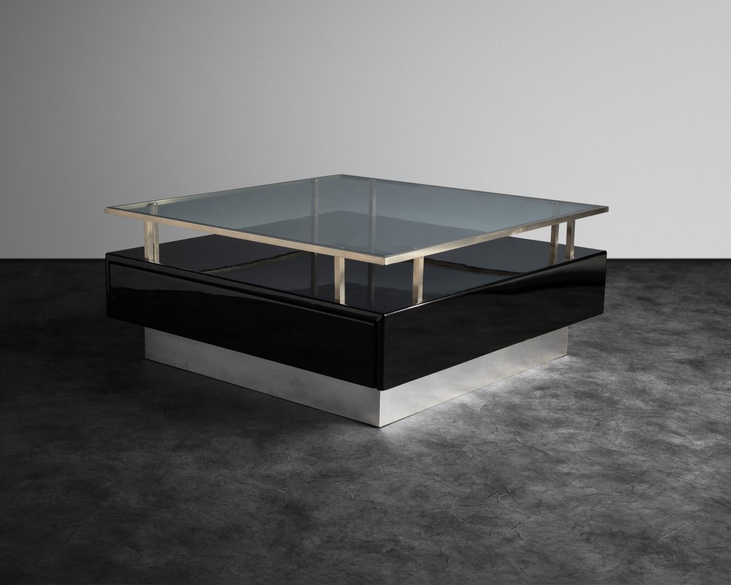 Quadratische, schwarz lackierte Tische mit einem erhöhten Aluminiumrahmen, der eine Glasplatte trägt. Die Tischgestelle sind mit einer geteilten Schublade ausgestattet.
 