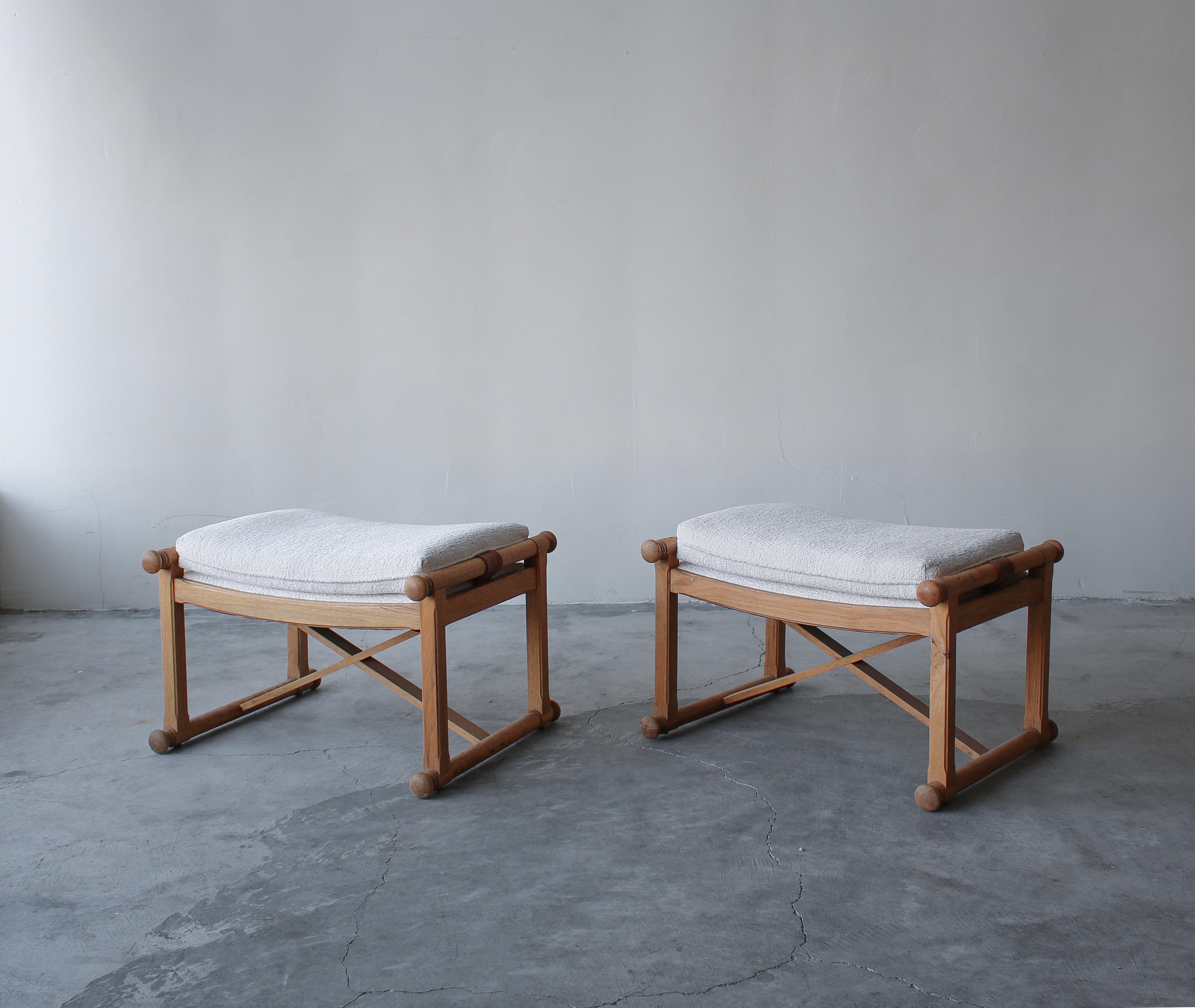 Just lovely pair of light oak stools with leather straps and bouclé style fabric. The stools feature an X-base style stretcher adding to their design details. This pair has a very warm organic yet in style feel to them. They are perfect for dressing
