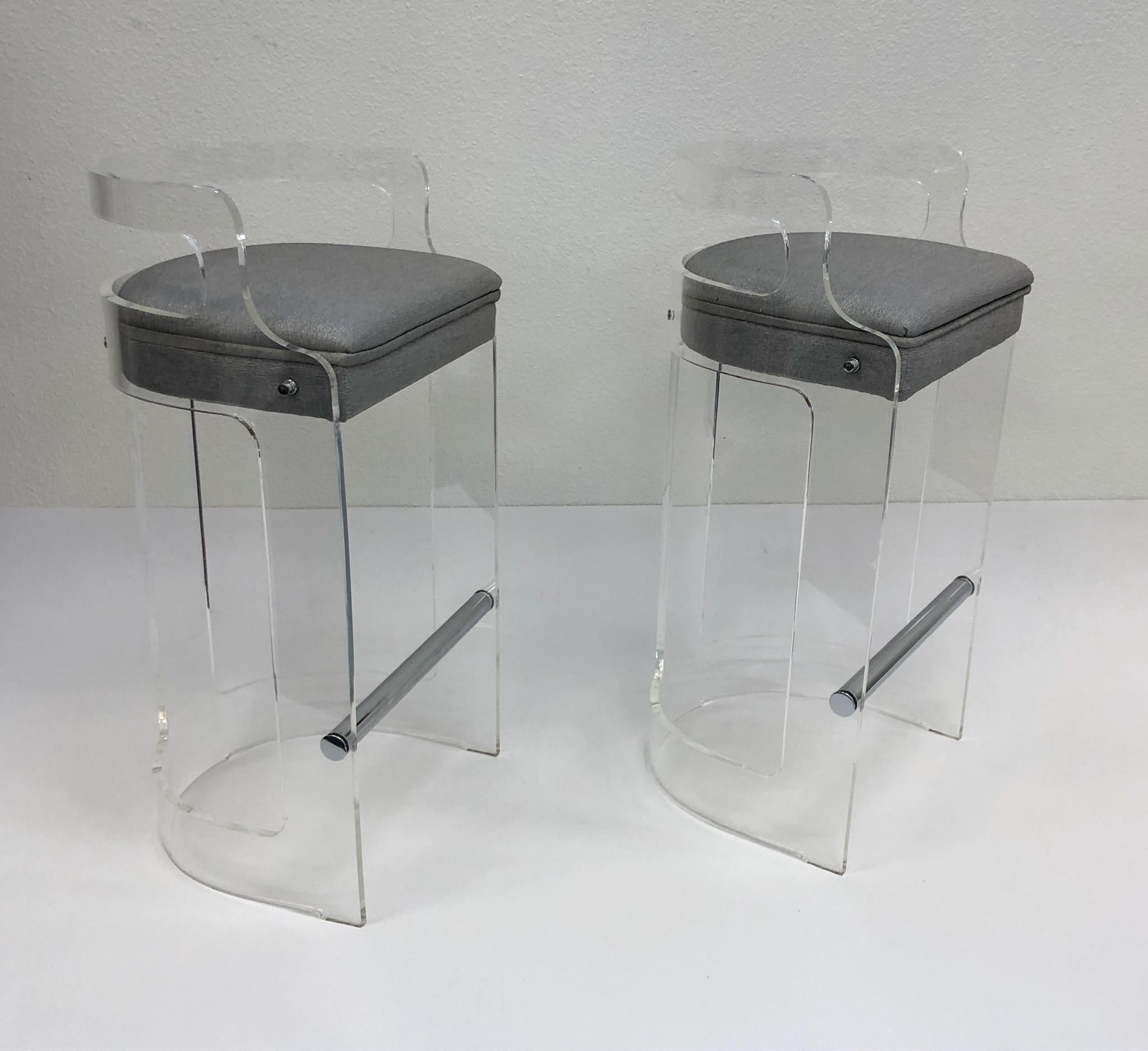 A glamorous pair of clear acrylic and polish chrome barstools design in the 1980s by Hill Manufacturing Co. The seat is covered in light grey with some metallic threads. 

Dimensions: 34” high, 29” seat, 18” wide, 16” deep.
