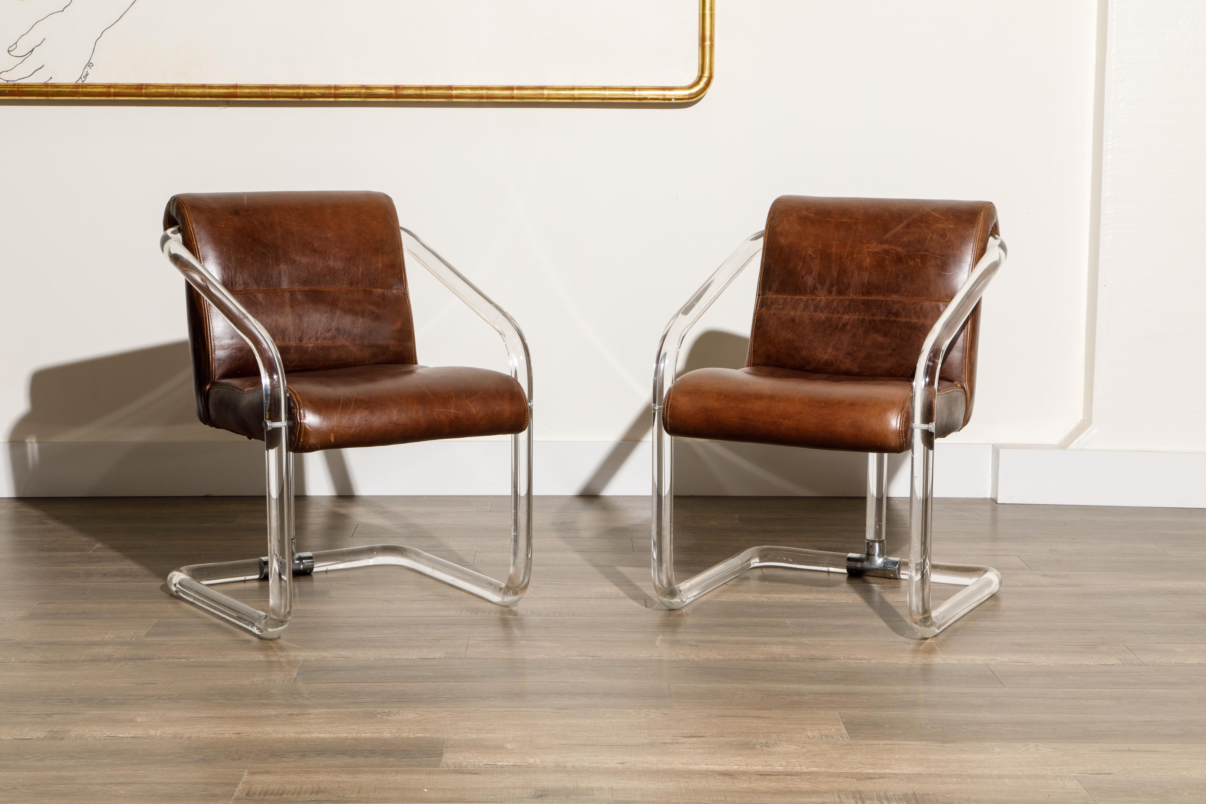 This gorgeous pair of lucite, leather and chrome armchairs by Lion in Frost (both chairs are signed), circa 1970s, are signed on the lucite post near the base and are in good vintage condition with lightly patinated and thick brown colored leather.