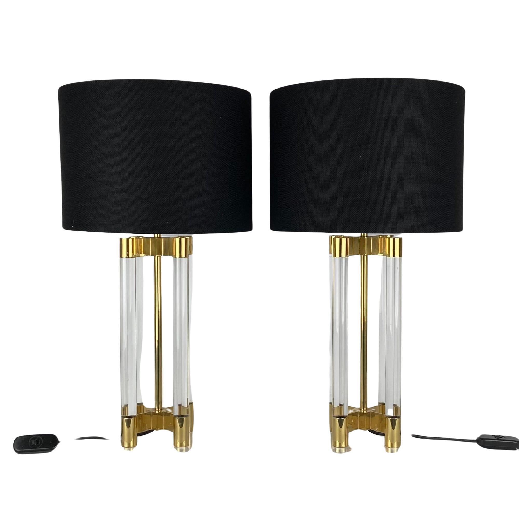 Pair of table lamps in transparant cylinders in lucite, held together by a base and top in brass. In the center is a brass pipe with the fitting on top of it.
Black fabric shades.