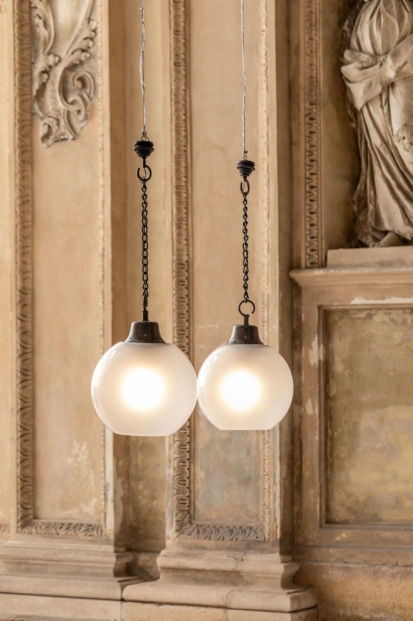 Incredible pair of LC10 pendants by Luigi Caccia Dominioni, provided with glass spherical shade and dark gray metal chain.