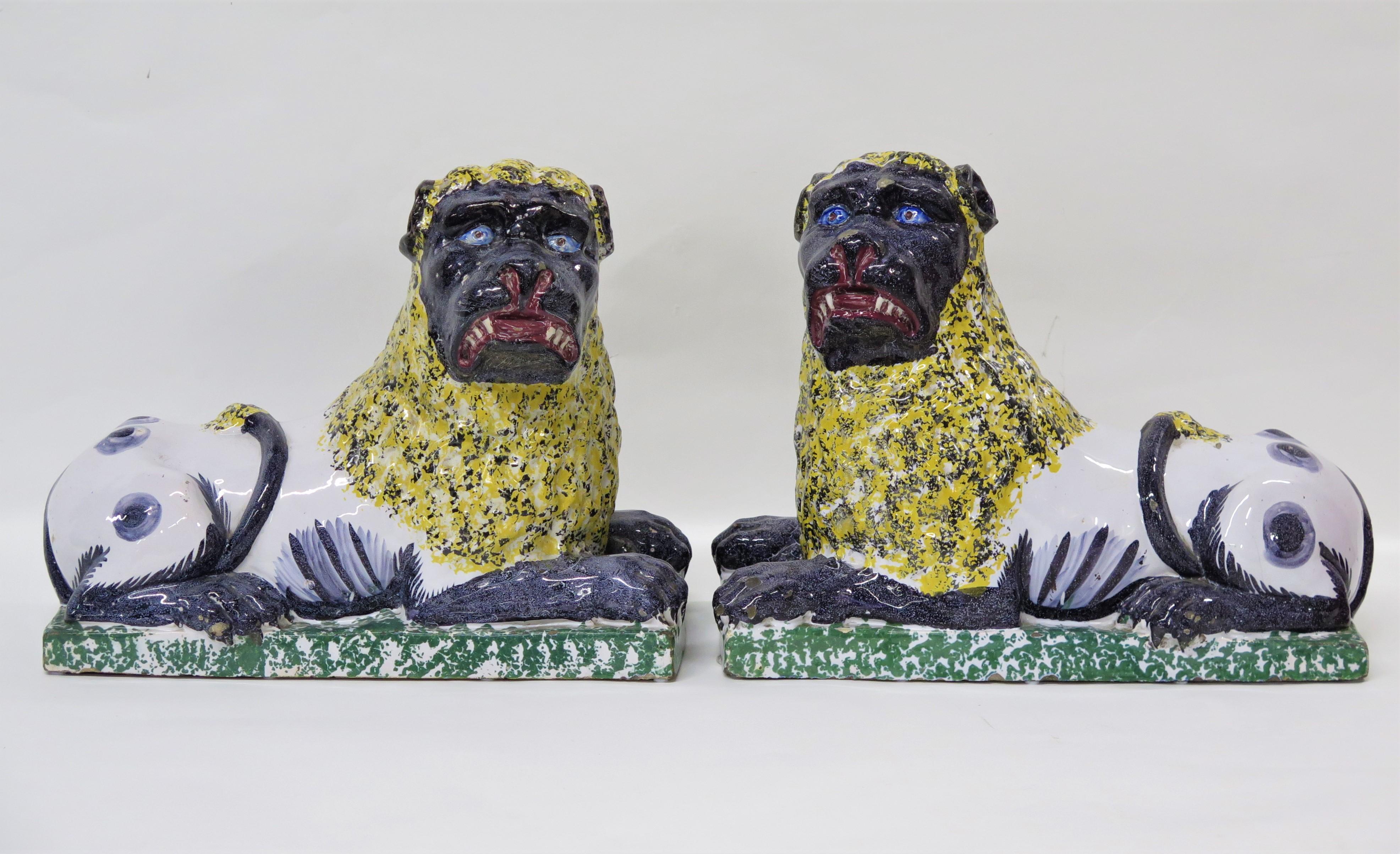 une grande paire de lions en faïence de Lunéville, chacun reposant sur un socle vert épongé, la queue enroulée sur le dos, leurs pattes, pieds, queues et visages sont peints en gris-bleu et leurs corps blancs ont des taches/marques gris-bleu, avec