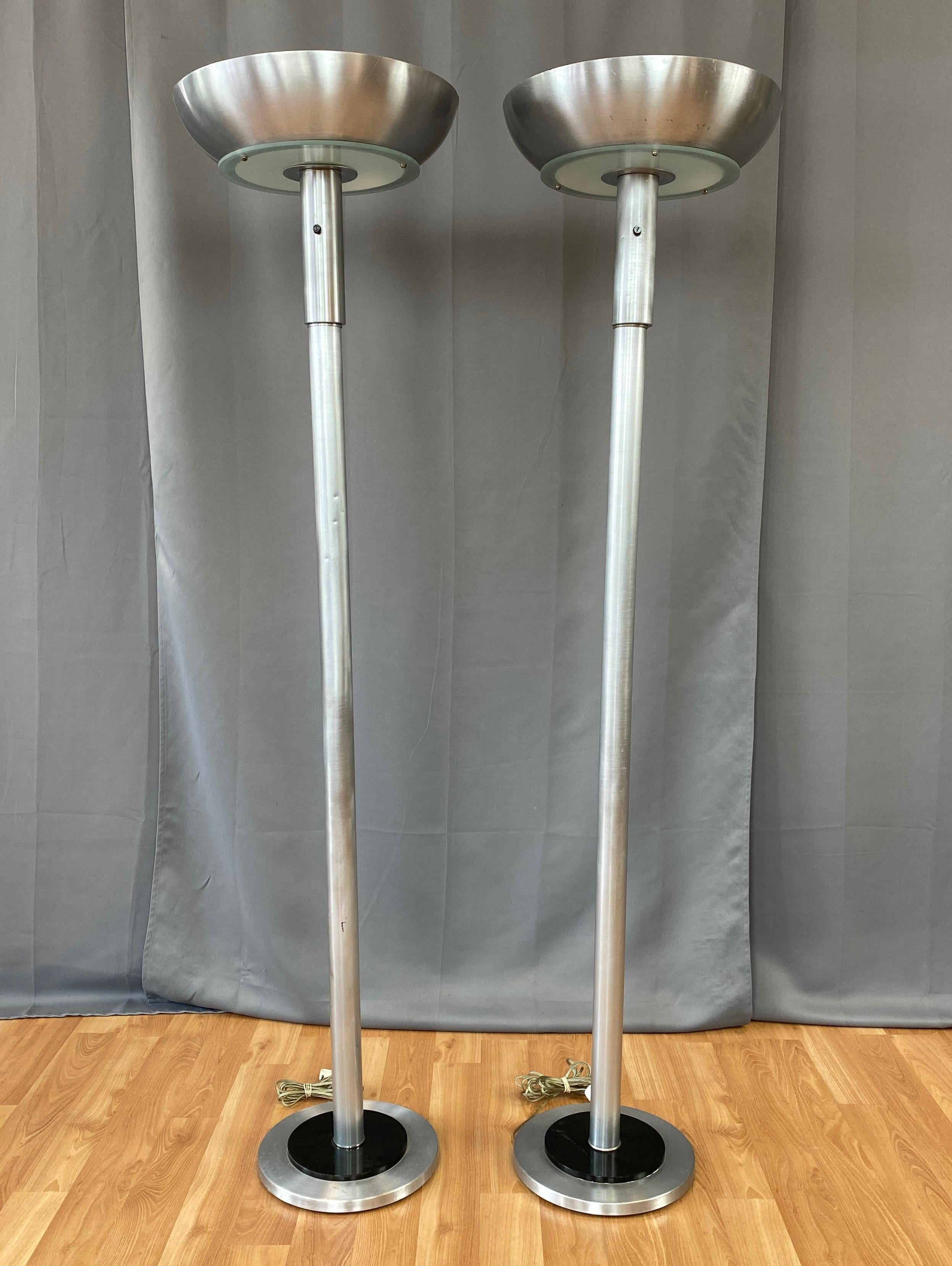 A handsome pair of uncommon mid-1940s Russel Wright-style Machine Age or Art Deco aluminum torchiere floor lamps.

Broad and deep spun aluminum bowl top with open bottom upon a frosted glass diffuser. Well-proportioned spun and brushed aluminum