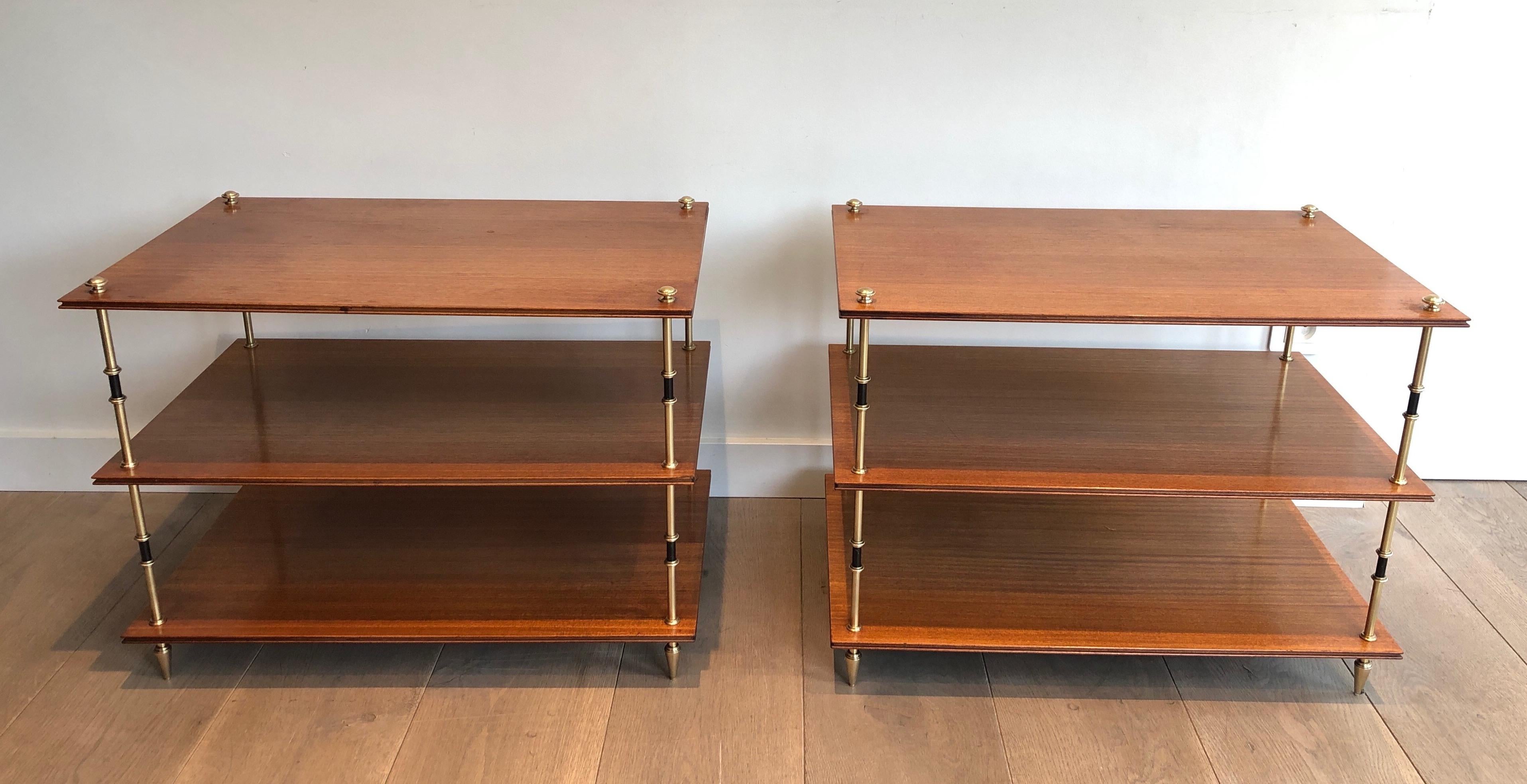 This very nice and rare pair of three tiers consoles or side tables is made of mahogany and brass. The tables are composed of 3 mahogany shelves that are worked all around and of 4 stylished feet with a black lacquered element on their center. This