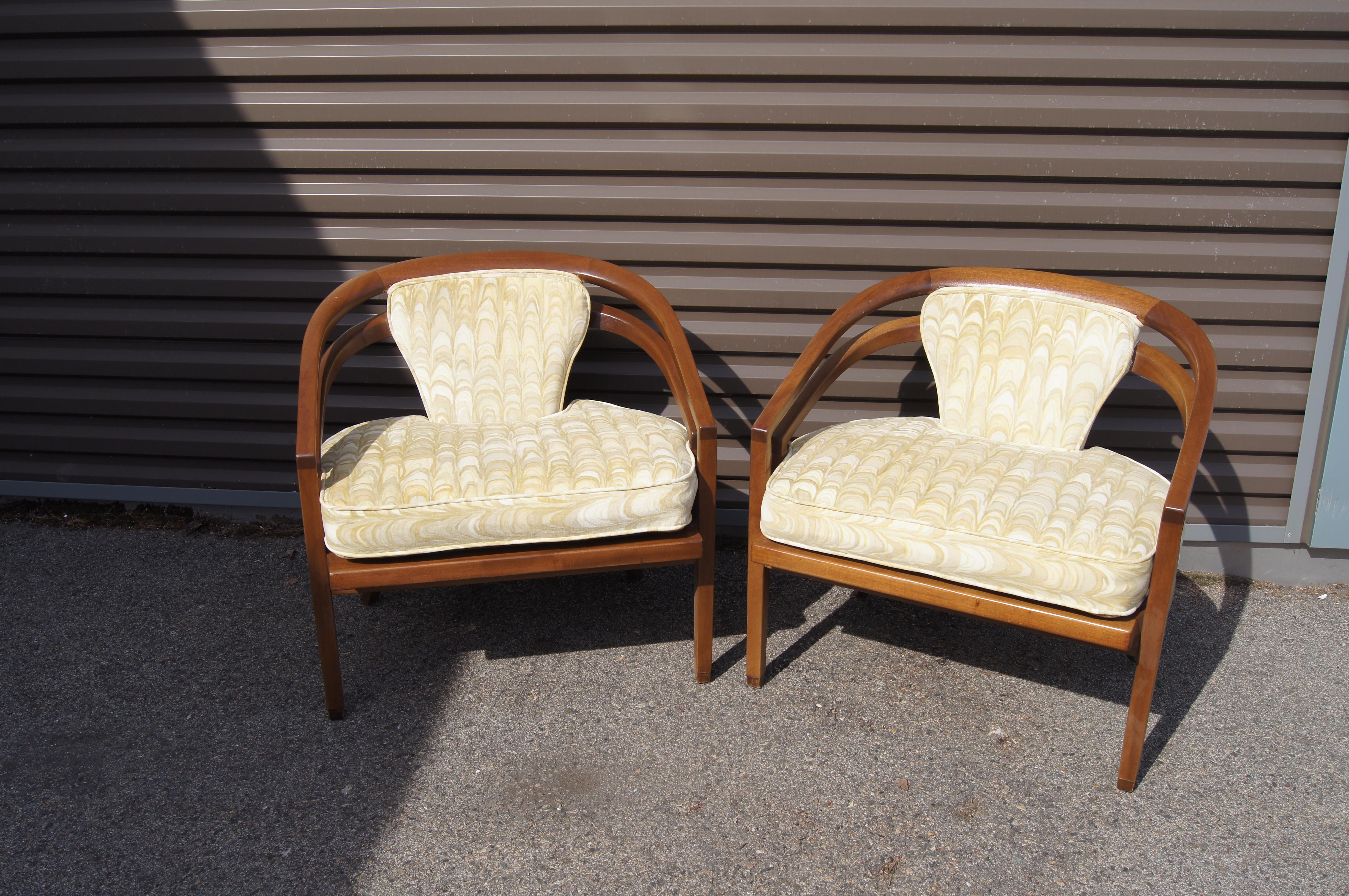 From the Baker Furniture Company, this pair of capacious mid-century armchairs features wide curved frames of mahogany loosely inspired by the Far East. The seat and center backrest are upholstered in a textile by Jack Lenor Larsen. The feet are