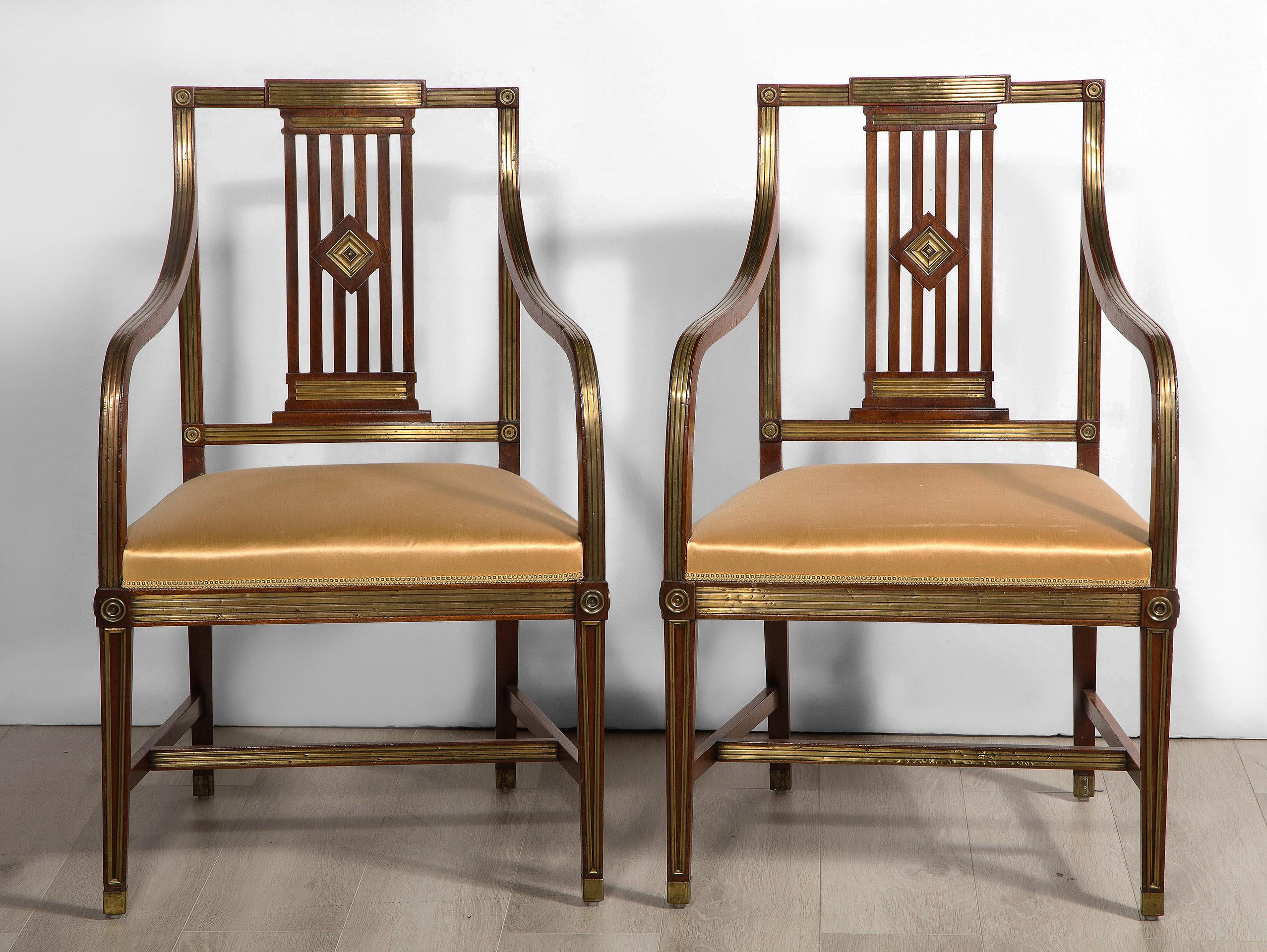 Each Russian neoclassical mahogany arm chair with an open fretwork back, having arms extending out and curving down to an upholstered seat over tapered legs with stretcher. The whole brass mounted.