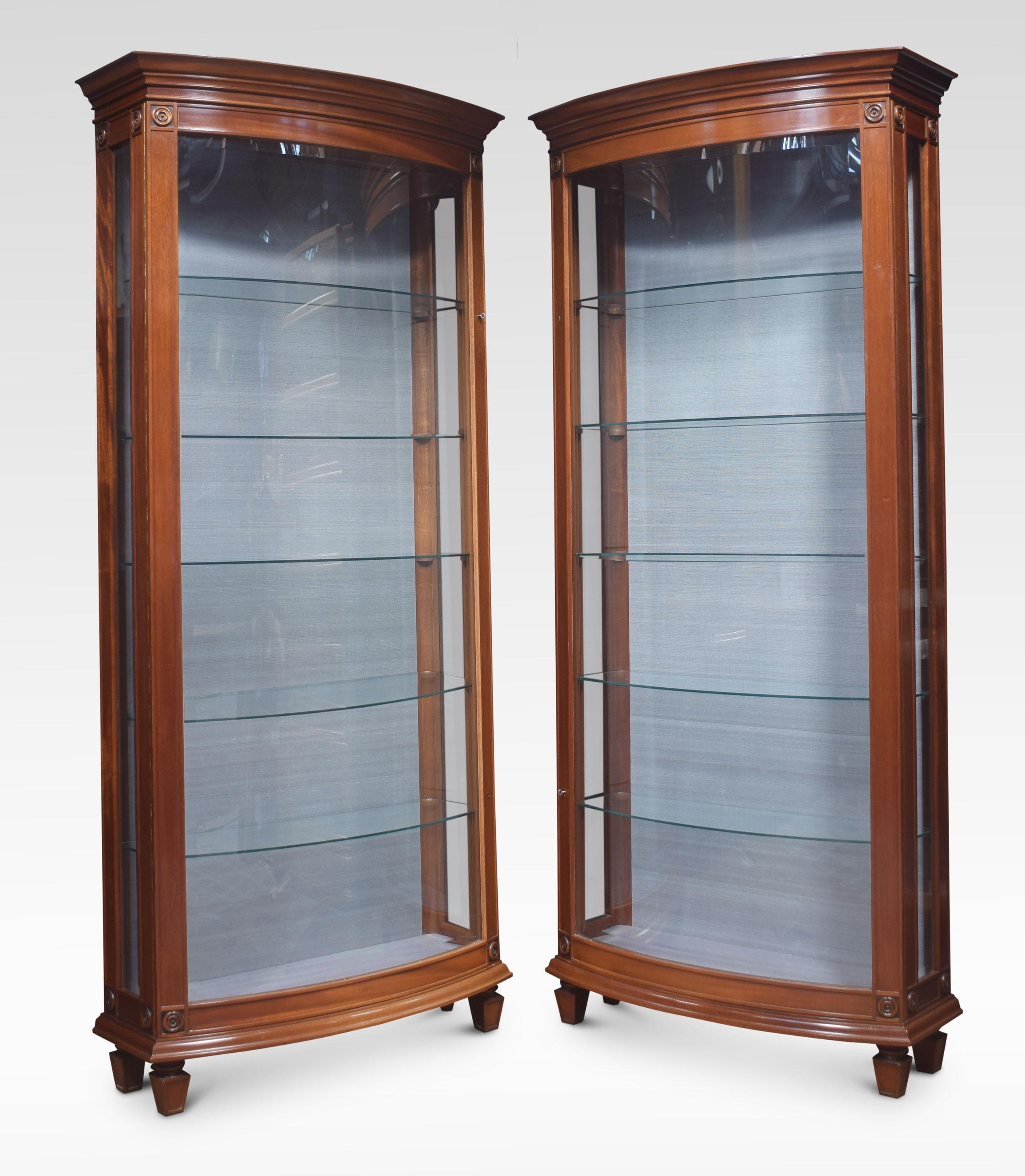 A pair of mahogany bow fronted glazed display cabinets, with a moulded cornice over a large curved beveled glass door, flanked by beveled glazed sides. The large doors opening to reveal silk upholstered interior and five glass shelves. All raised