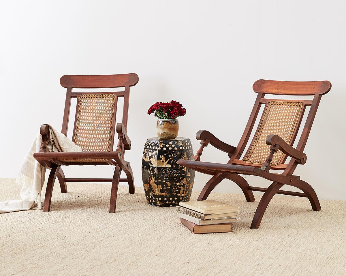 Unique pair of mahogany and cane folding armchairs or plantation chairs made in the campaign style. Featuring hand caned seats and back with graceful curved legs and arms. Very comfortable ergonomic seats with sturdy arms supported by small turned