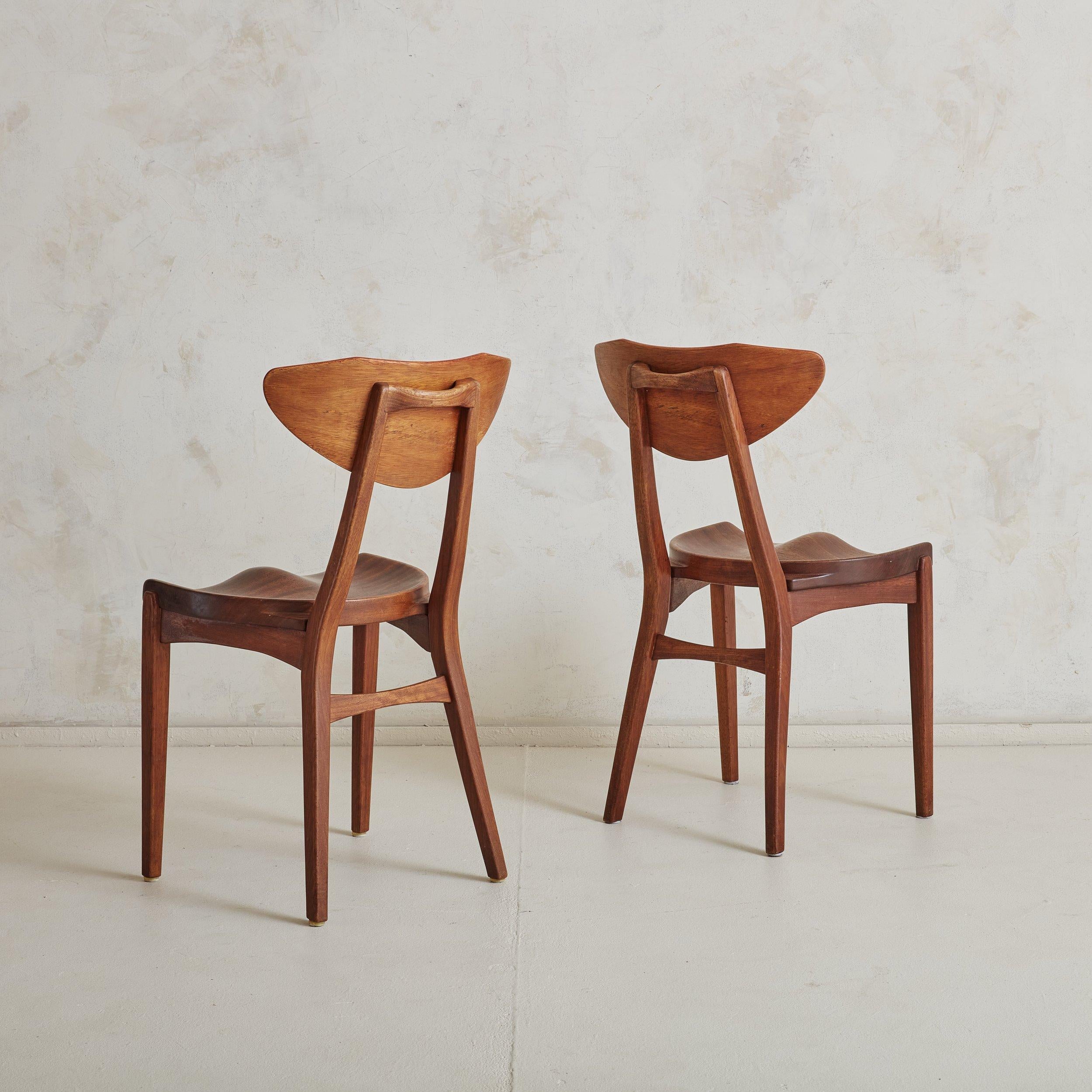 A pair of Danish Modern dining chairs designed by Richard Jensen & Kjærulff Rasmussen featuring sculptural frames constructed of rich, dark brown mahogany with stunning graining and natural patina. Carved seats catch the eye while also providing