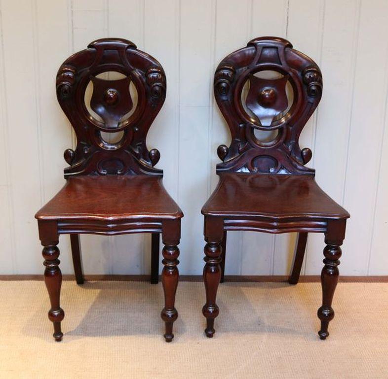 Pair of mahogany hall chairs, having carved shield backs standing on turned legs at the front and splayed legs to the back.