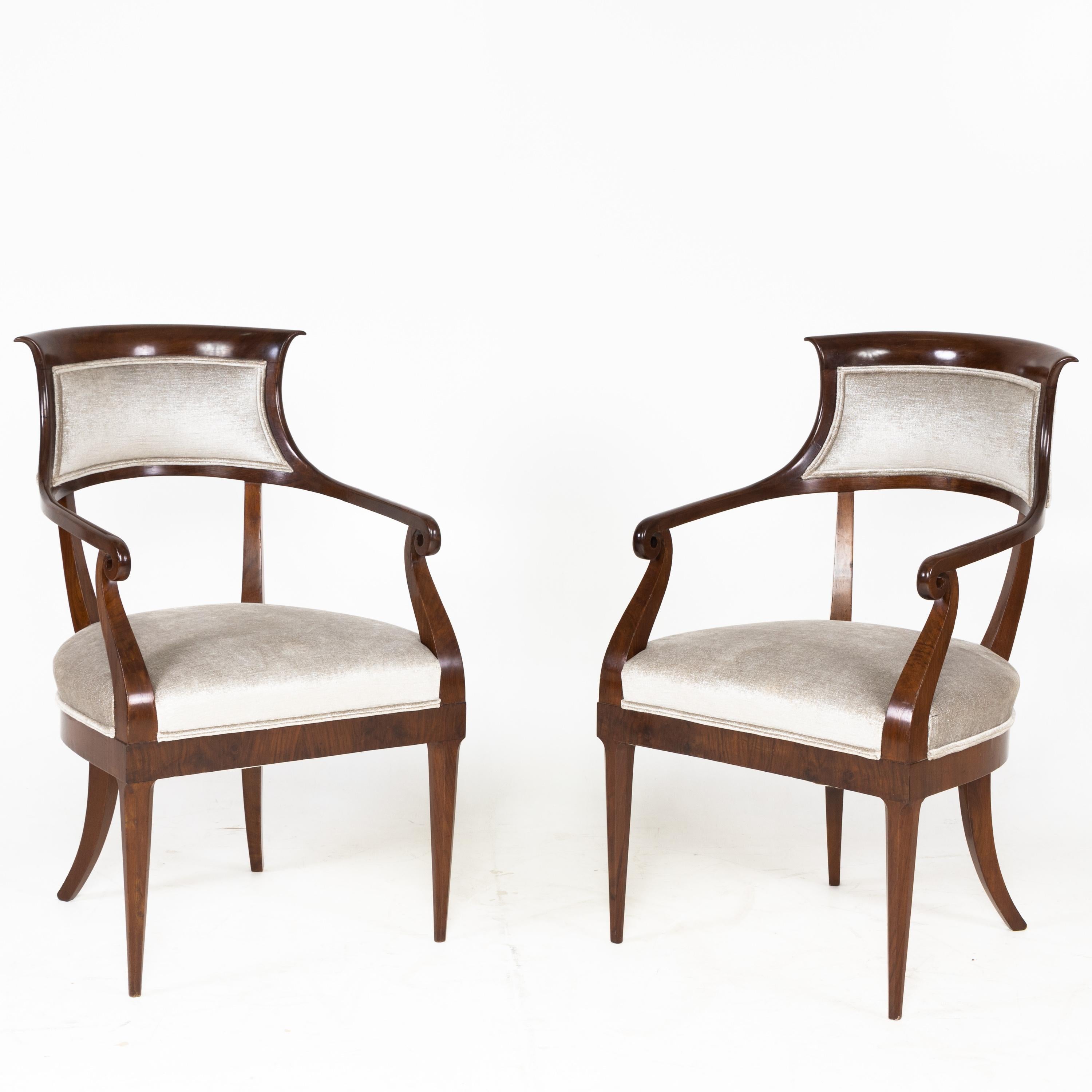 Pair of Italian Mahogany armchairs standing on octagonal pointed legs in front and sabre legs in the back. The backrest with retracted sides and flared edge merges into the volute-shaped armrests. The straight frame ends flush with the curved