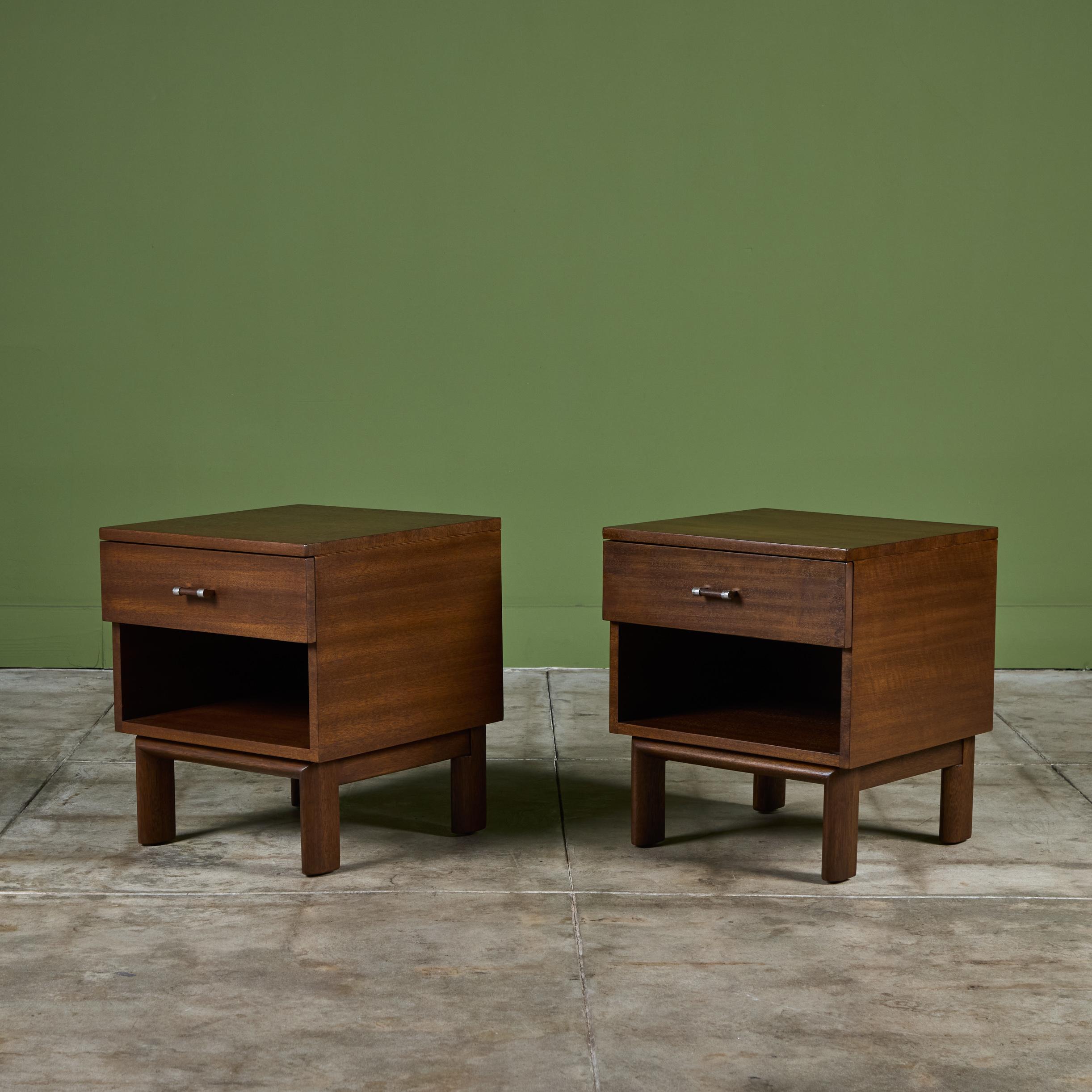 Pareja de mesillas de noche de caoba de John Keal para Brown Saltman, c.1950, EEUU. Este diseño minimalista presenta un cajón superior con tirador de madera y niquelado. Debajo hay un estante abierto para almacenamiento adicional junto a la cama.