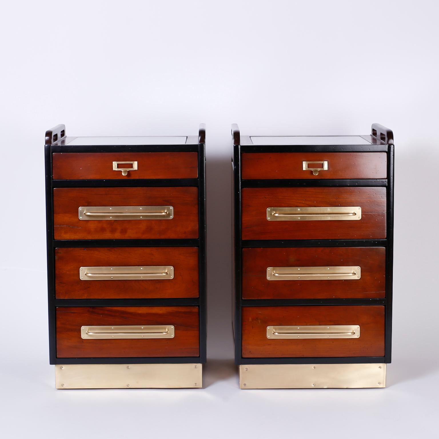Handsome pair of nautical style mahogany nightstands with a distinctive yacht like ambiance. Featuring cut out handles and a glass insert at the top, four drawers with brass hardware, paneled sides, and a brass kick plate base slightly raised on