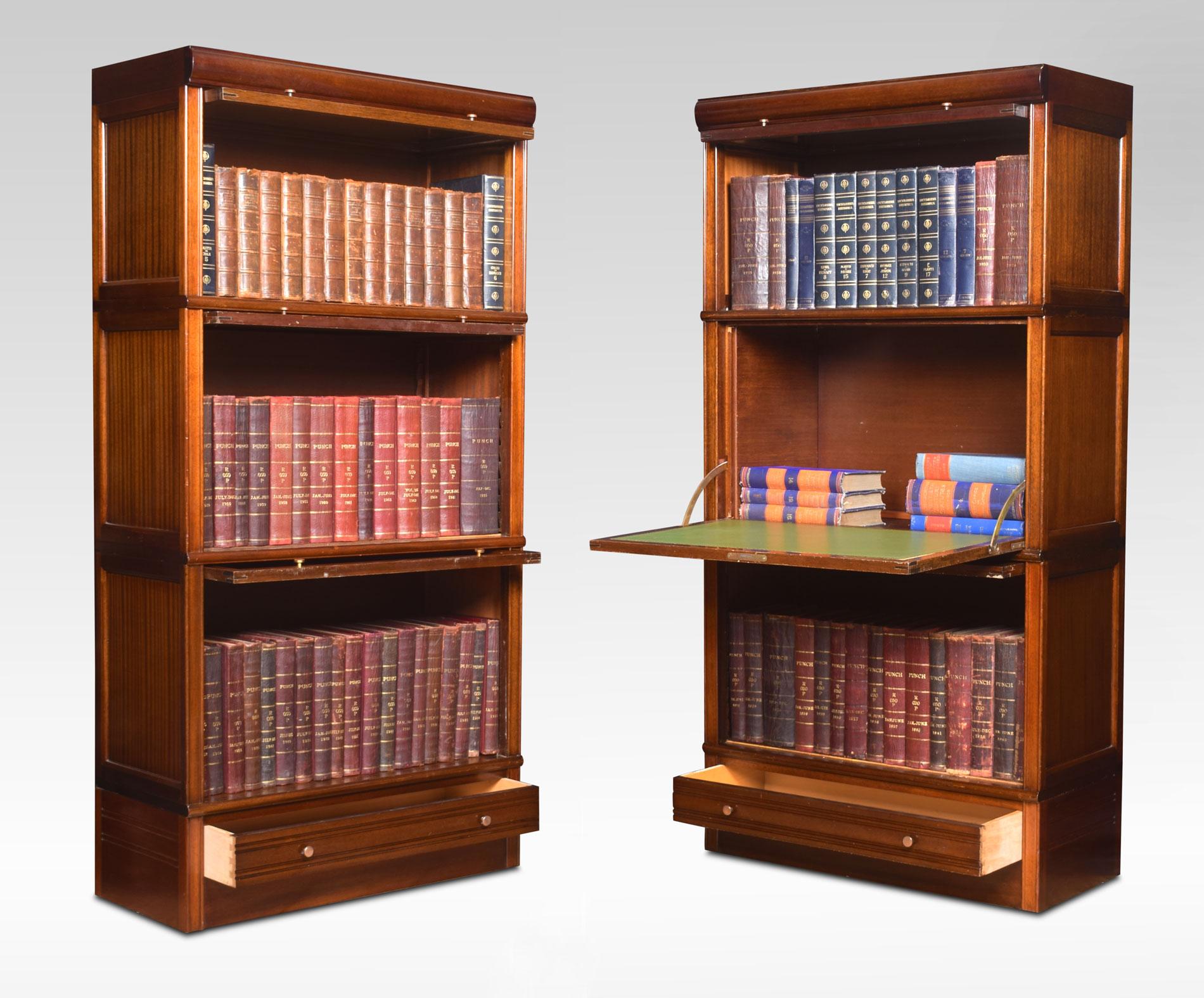 Pair of mahogany sectional bookcases. The moulded top above glazed doors and brass knobs, the next two sections having mahogany panelled doors one section fitted with inset green leather writing surface. To the base fitted with a single long