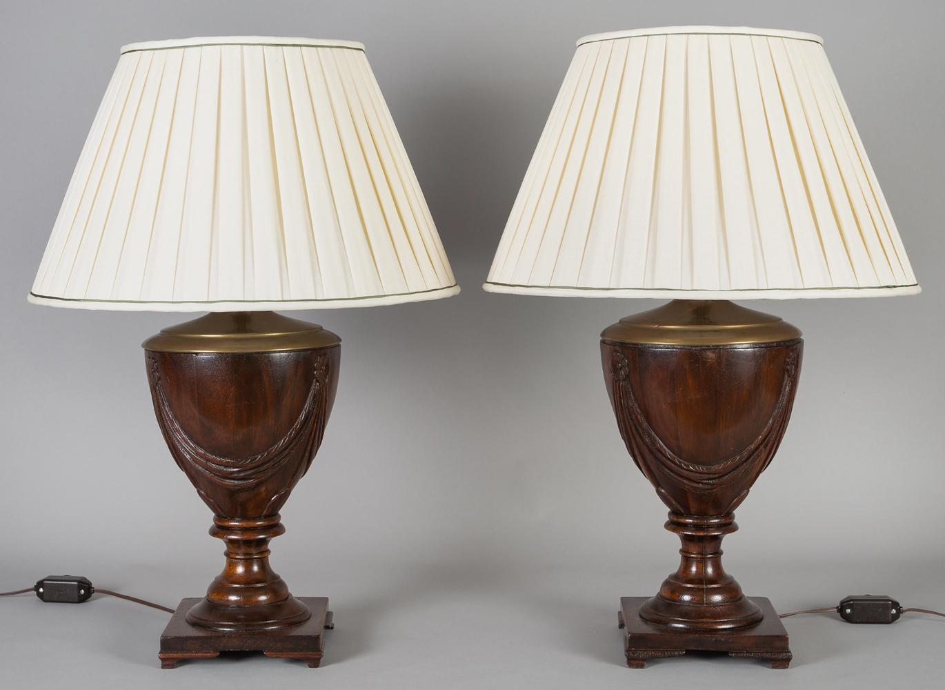 Pair of Georgian style mahogany urn shaped lamps, each with carved rosettes and swag decoration, pleated shades, mounted on turned pedestal and square bases with bracket feet.