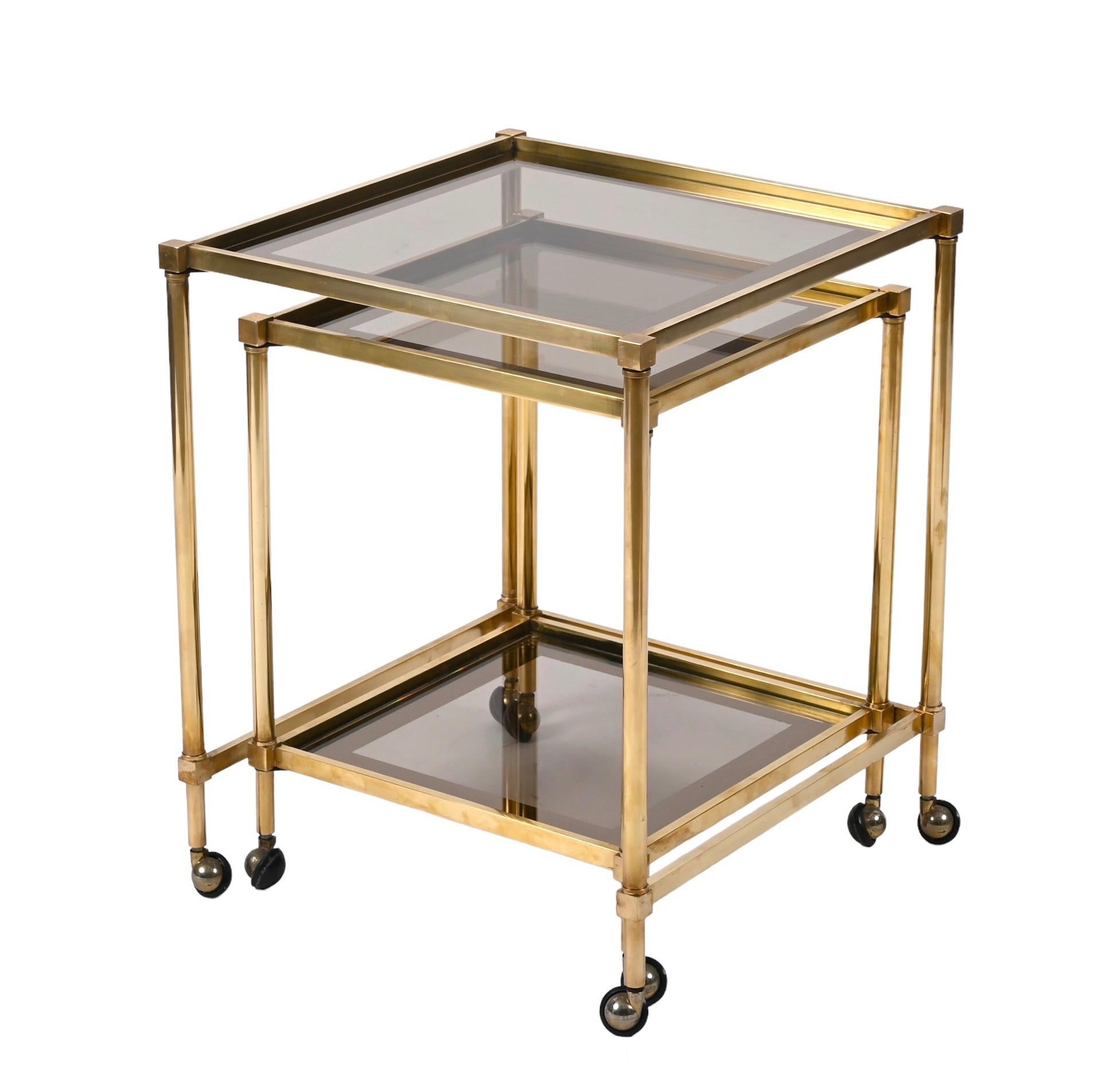 Set of two brass mirrored borders with glass top nesting tables. Maison Jansen designed this fantastic set in France during the 1970s.

This set is made of two small tables with retractable interlocking wheels, glass shelves and a mirror edge and