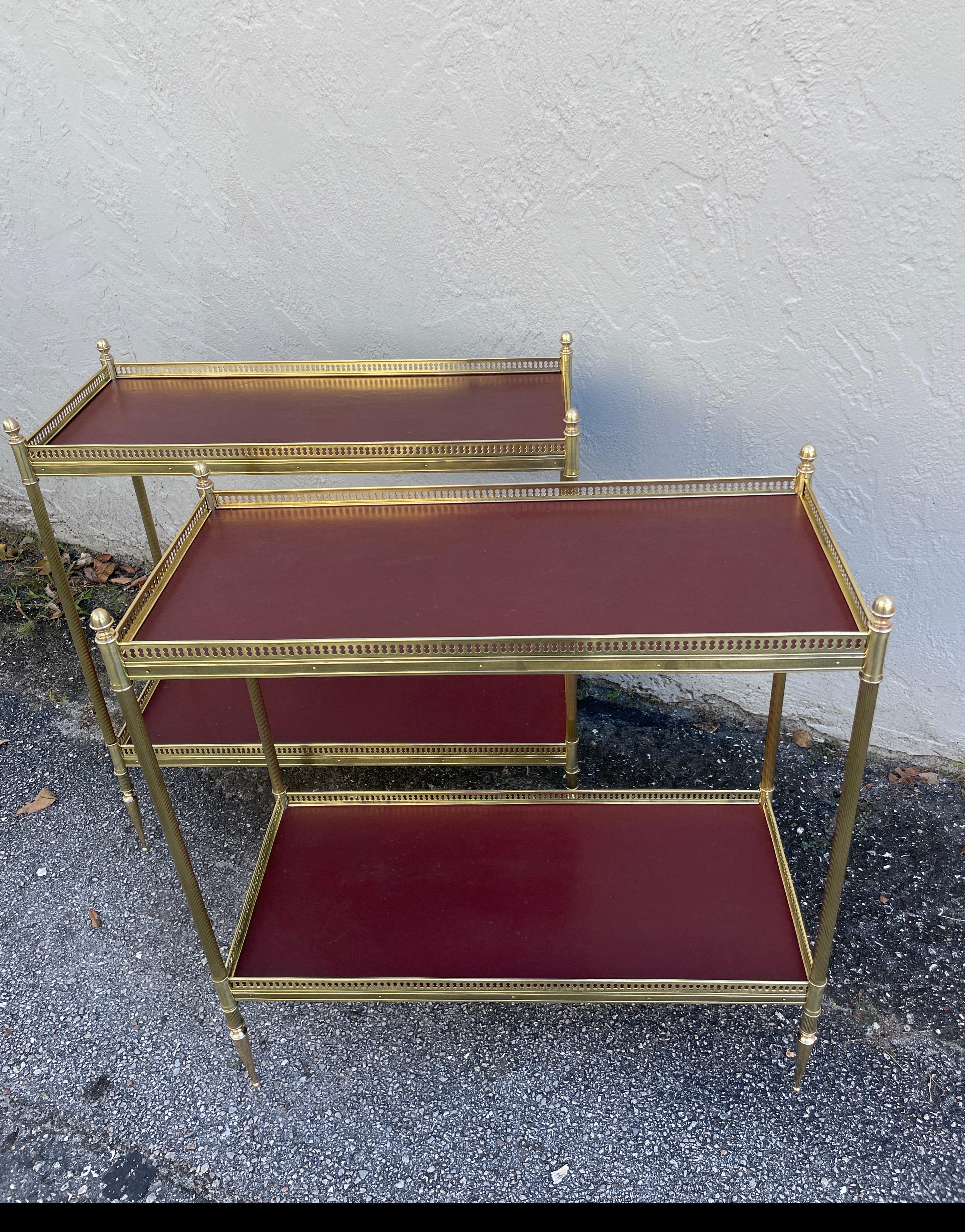A rare pair of Maison Jansen Two-tiered brass side tables with red leather surfaces. 