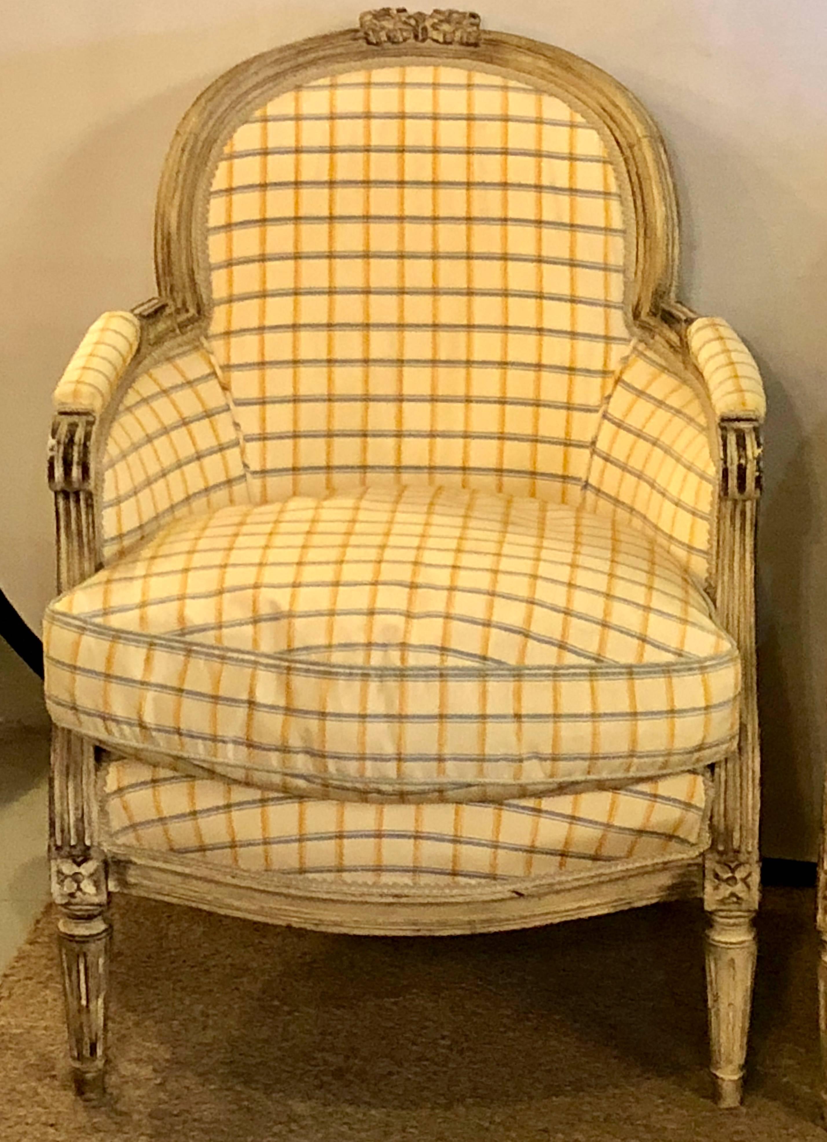 Pair of Maison Jansen Louis XVI style bergere chairs in a Burberry fashioned fabric. These fine antiqued paint decorated bergere chairs depict this iconic designers flare for fashion at the firms highest peek. The worn and weathered frames in an off