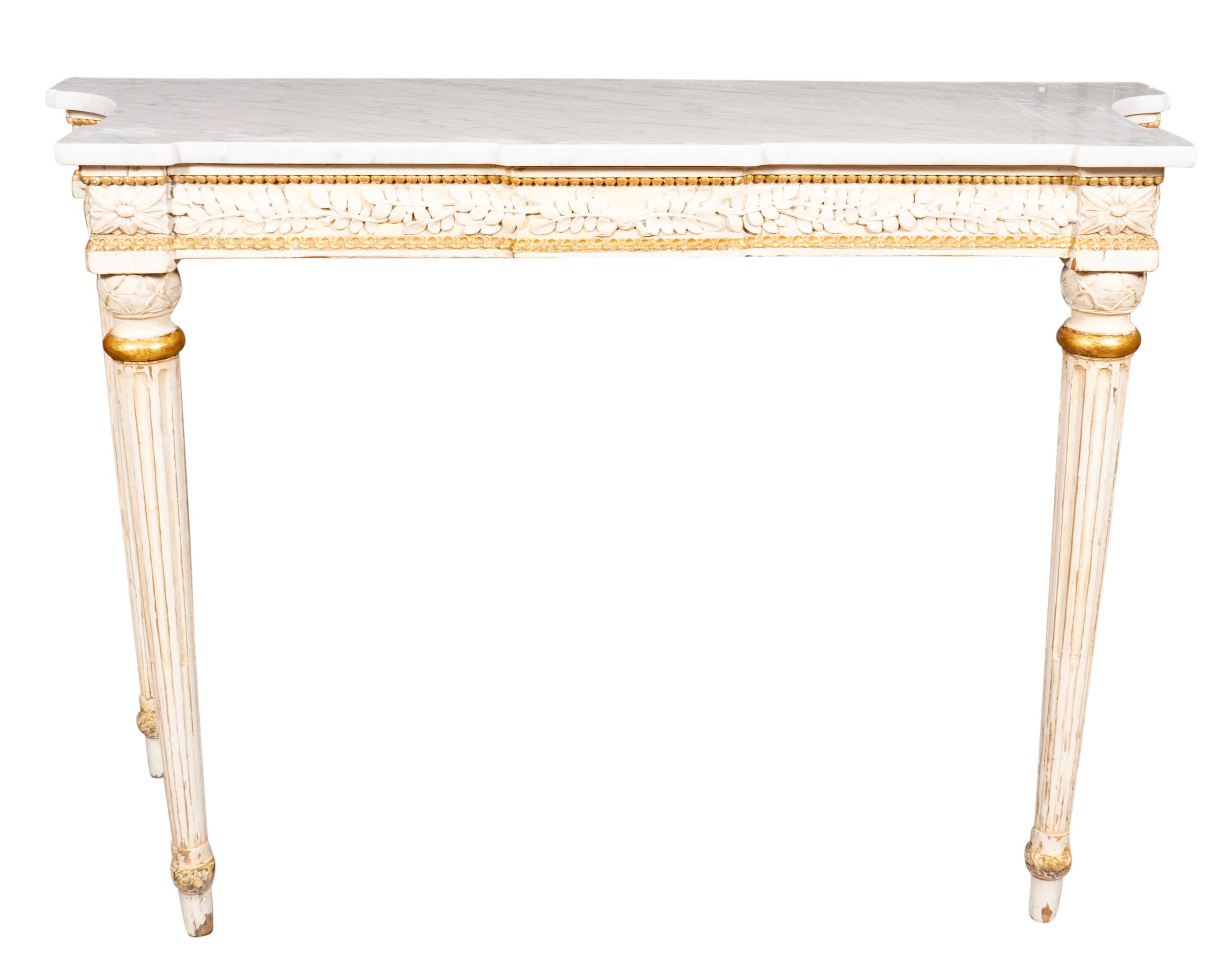 With rectangular white Carrara marble tops with a conforming creme painted frieze with finely carved leaves. Raised on circular tapered fluted legs with a touch of gilding at top of legs. With metal labels on back 