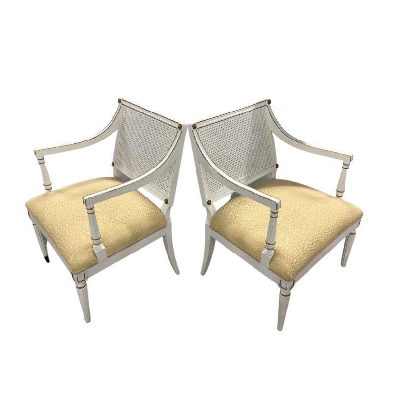A pair of Maison Jansen style Louis XVI painted arm chairs with cane backs and upholstered yellow seats. Chairs are painted white with square backs and seats and legs and arms are fluted. Gilt detail is elegantly applied to frame back, arms and