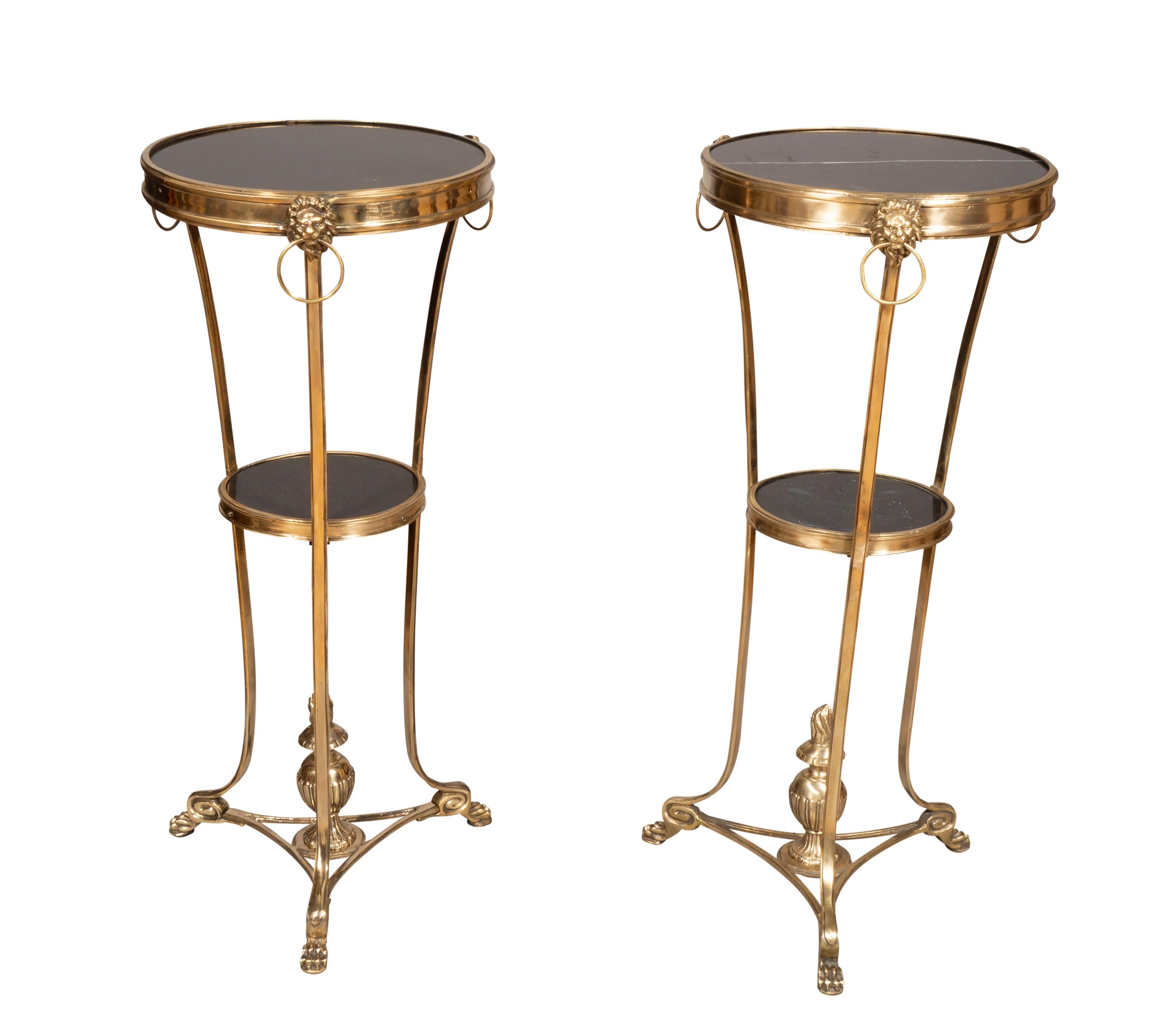 Each with a circular top with black marble insert with a brass border with lions head rings. Lower conforming shelf. Bottom finial ending on paw feet.