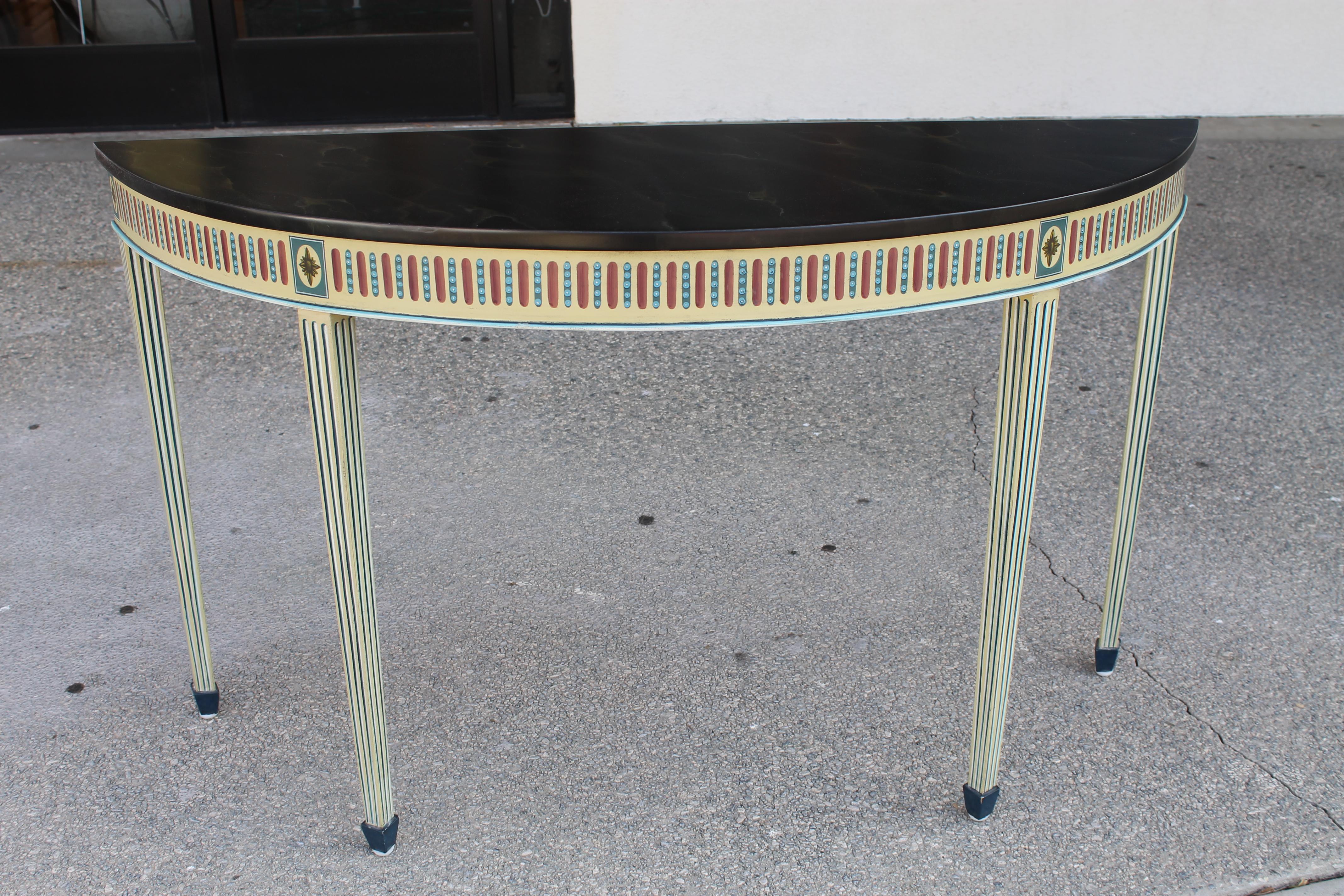 A pair of Maitland Smith neoclassical style console tables, each having a demi-lune top, above polychrome decorated tapered legs. The tops have a hand painted faux finish with clear lacquer.  Underneath each table is signed HAND PAINTED Maitland
