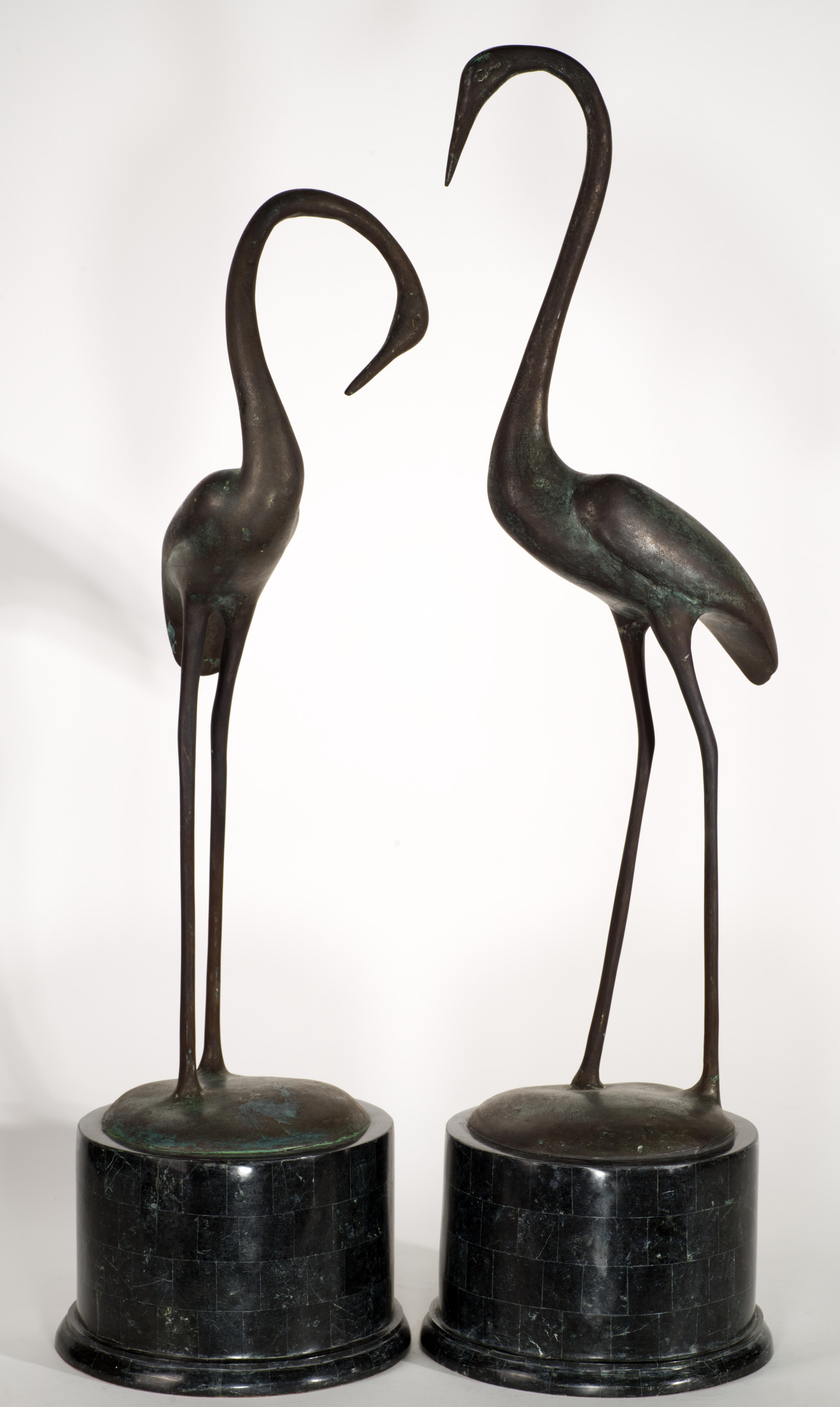 Coppia di grandi sculture vintage con figure di garzette in piedi rese in modo elegante. Gli uccelli sono realizzati in bronzo patinato con un leggero effetto verdastro; sono montati su importanti basi cilindriche in marmo nero con dettagli