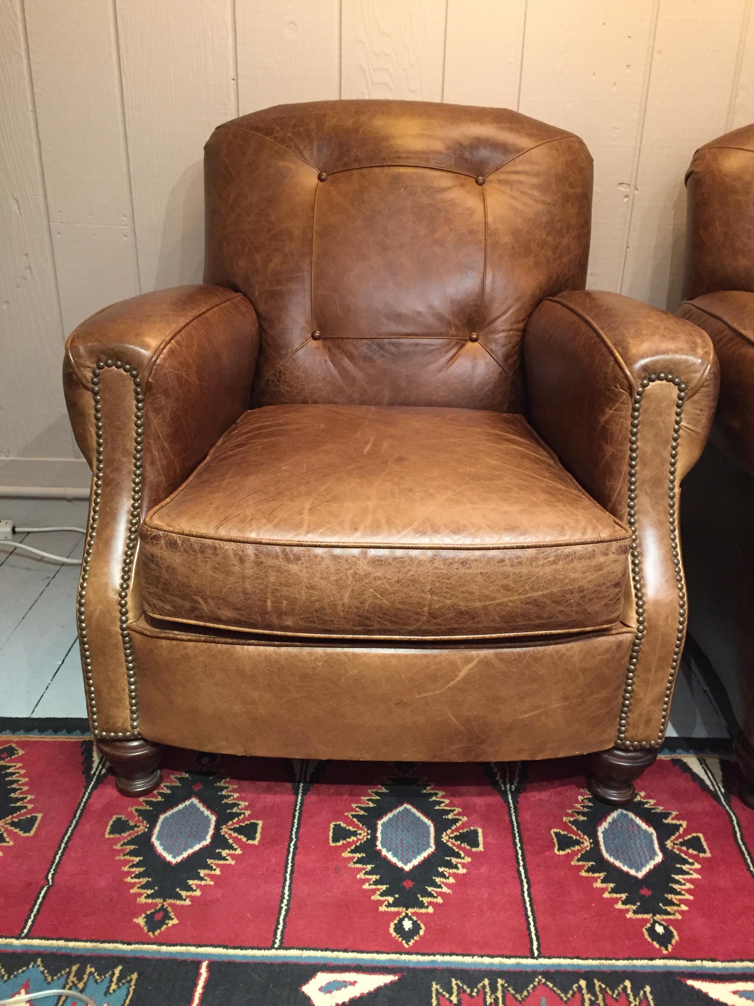 Impressive and masculine pair of beautifully distressed high grade leather club chairs having nailhead detailing and 4 subtle buttons on the backs. Beautiful from every angle and in excellent shape. Comfy too!