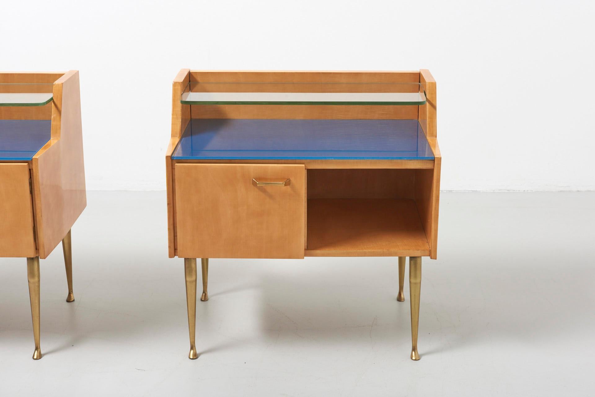 A pair bedside tables in maple with an original blue painted glass top, a glass shelf and brass feet.
Made in Italy in the 1950s.