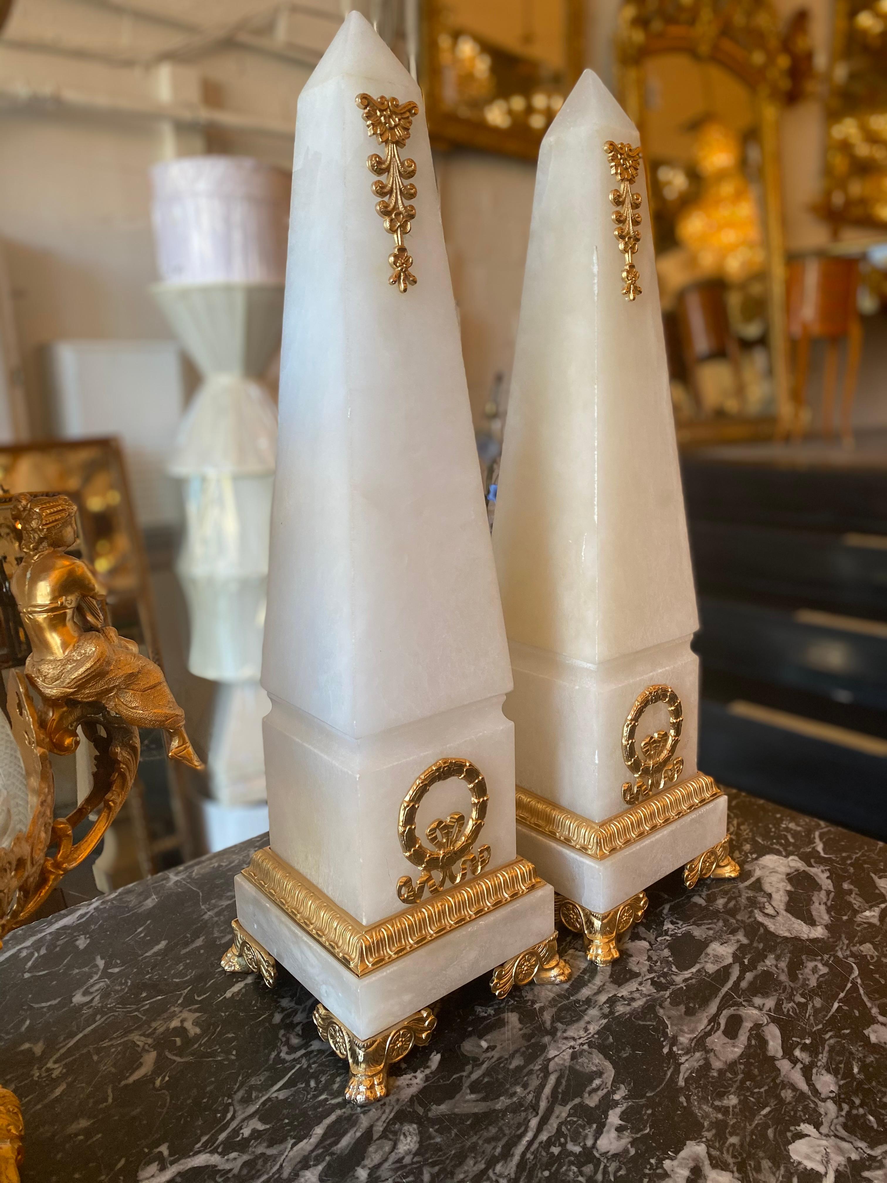 A pair of alabaster obelisks fitted along the bottom with gilt bronze bordering and lions feet, further fitted along the body with Cartouches and ribbon banners,
circa 20th century
Origin: Continental.