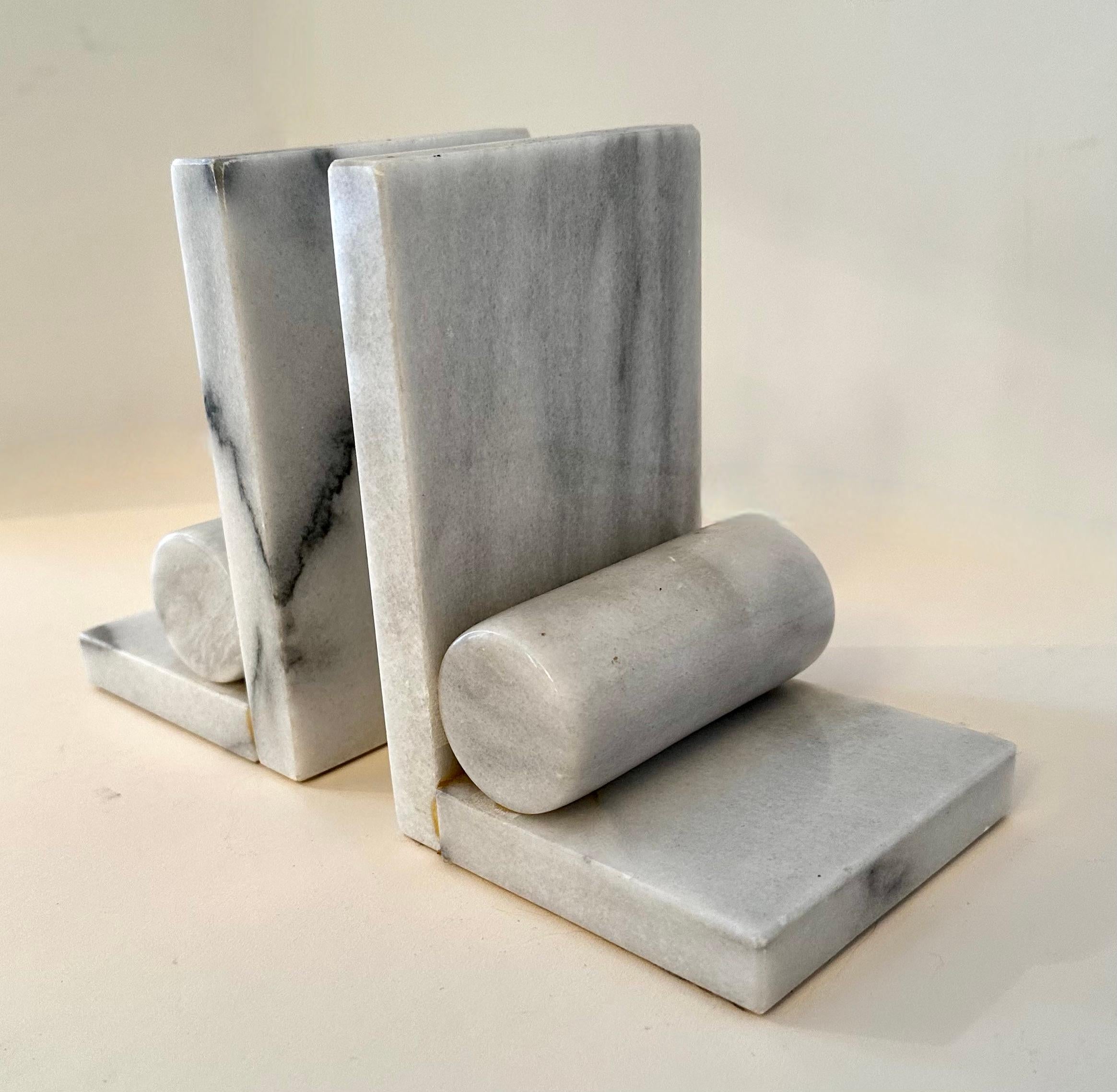 A lovely pair of Carrara marble bookends - two 90 degree angle pieces with a solid cylinder as a very nice and simple detail. 

The pair would be a complement to any desk, or work station. In the office, kitchen or den. A wonderful, heavy and