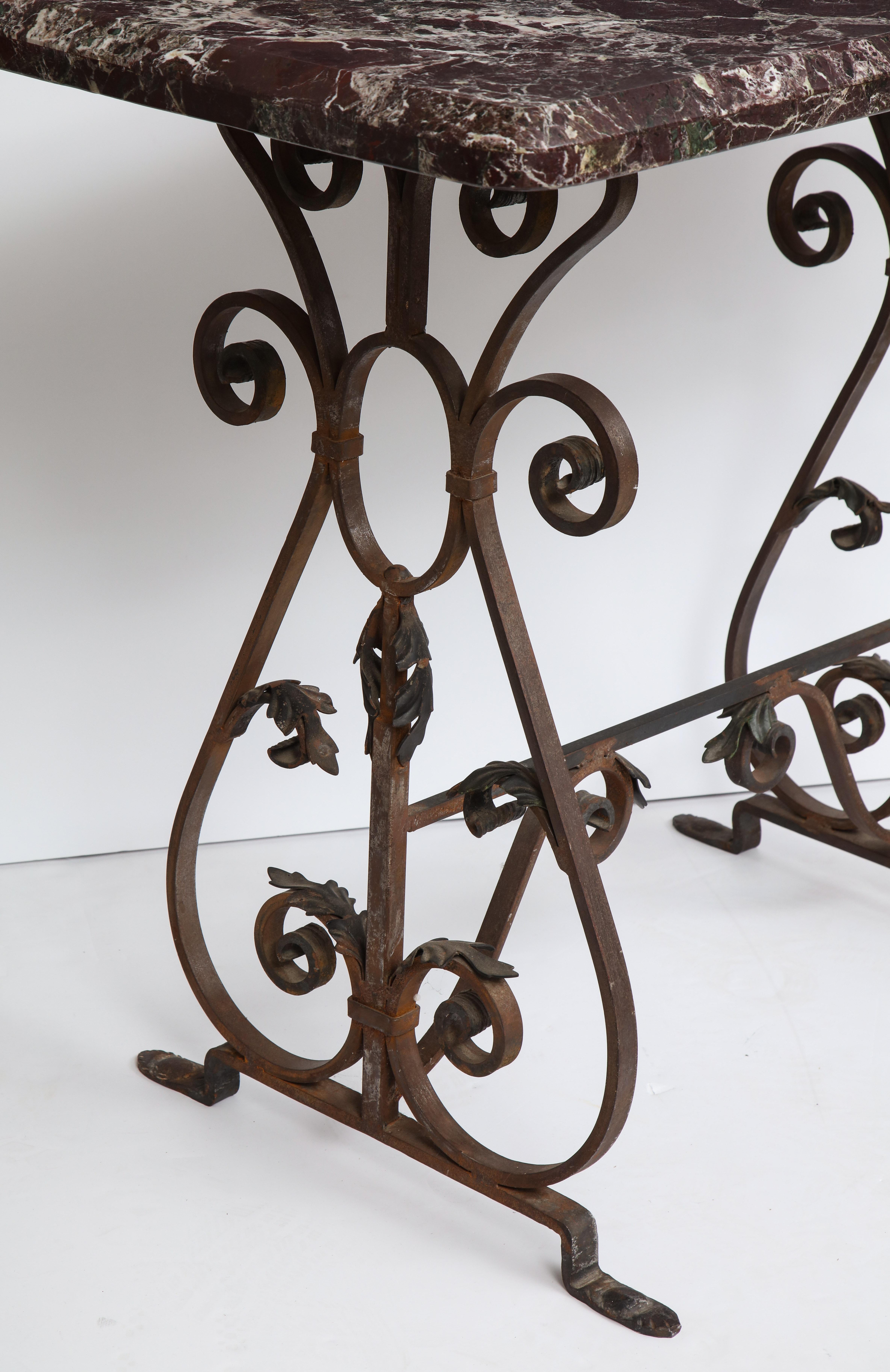 A pair of wrought iron console tables, each having marble tops supported on scrolling and foliate decorated bases.