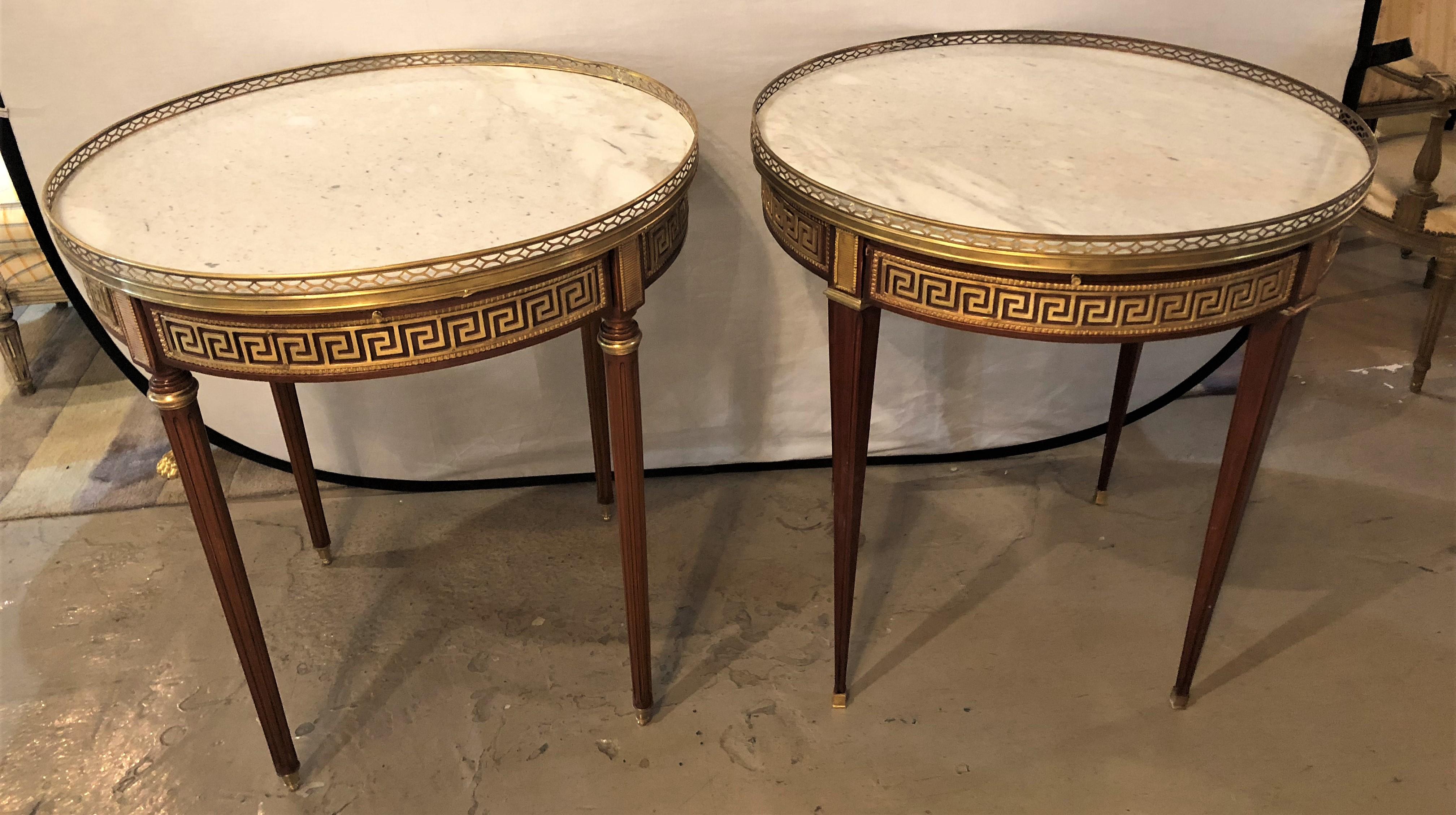 A pair of marble-top Greek key Bouillotte or end tables in mahogany with double drawers and pull-out slides. Each bronze sabot leading to a group of tapering legs terminating in bronze capitals supporting a apron have full Greek key design and