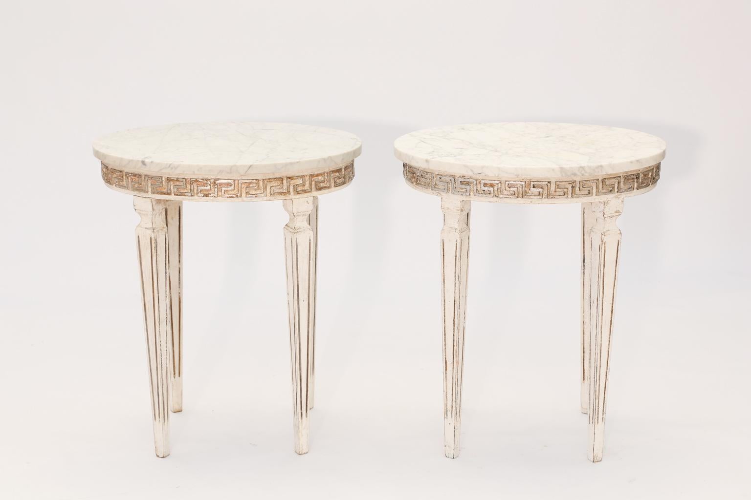 Pair of side tables, each having an oval top of Carrara marble, on painted and parcel silver gilt wooden base, its apron carved with Greek-key scroll, raised on four, square-section, fluted, tapering legs. 

Stock ID: D1603.