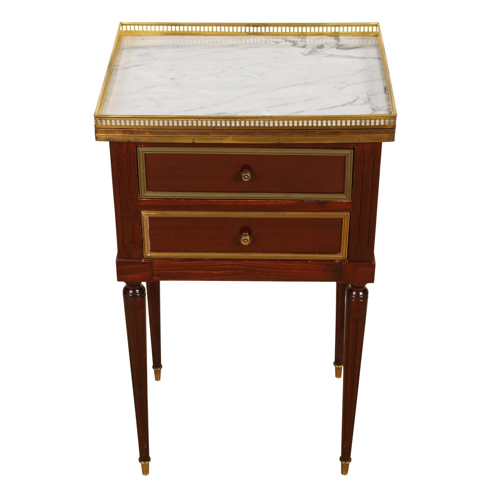 A pair of vintage traditional nightstands each with two drawers, a marble top with pierced brass gallery rail, brass trim on each drawer and reeded legs.