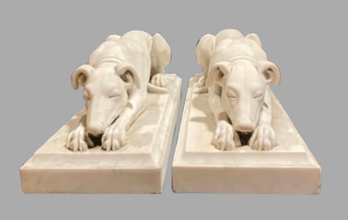 A fine pair of Neoclassical style white marble whippets, each well-carved animal in a resting position on a rectangular plinth. These sculptures have an attractively weathered patina coming from a Bay Area estate where they graced the entry of an