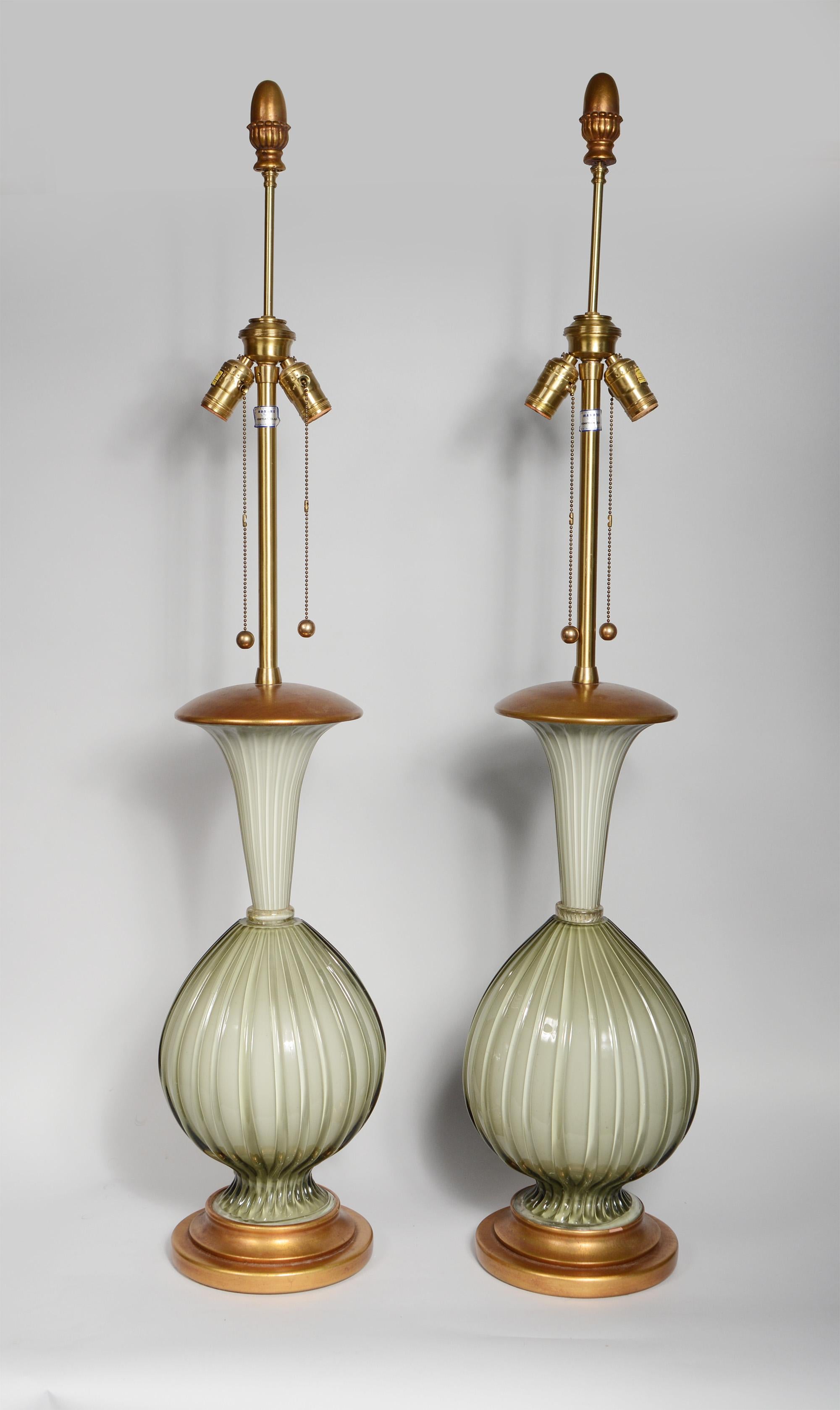 Pair of tall Venetian glass table lamps by Marbro Lamp Company. These have a warm grey ribbed glass cased over white. They have gilt wood bases and caps. The gilt finials are original. There is a small loss of paint on the base of one.