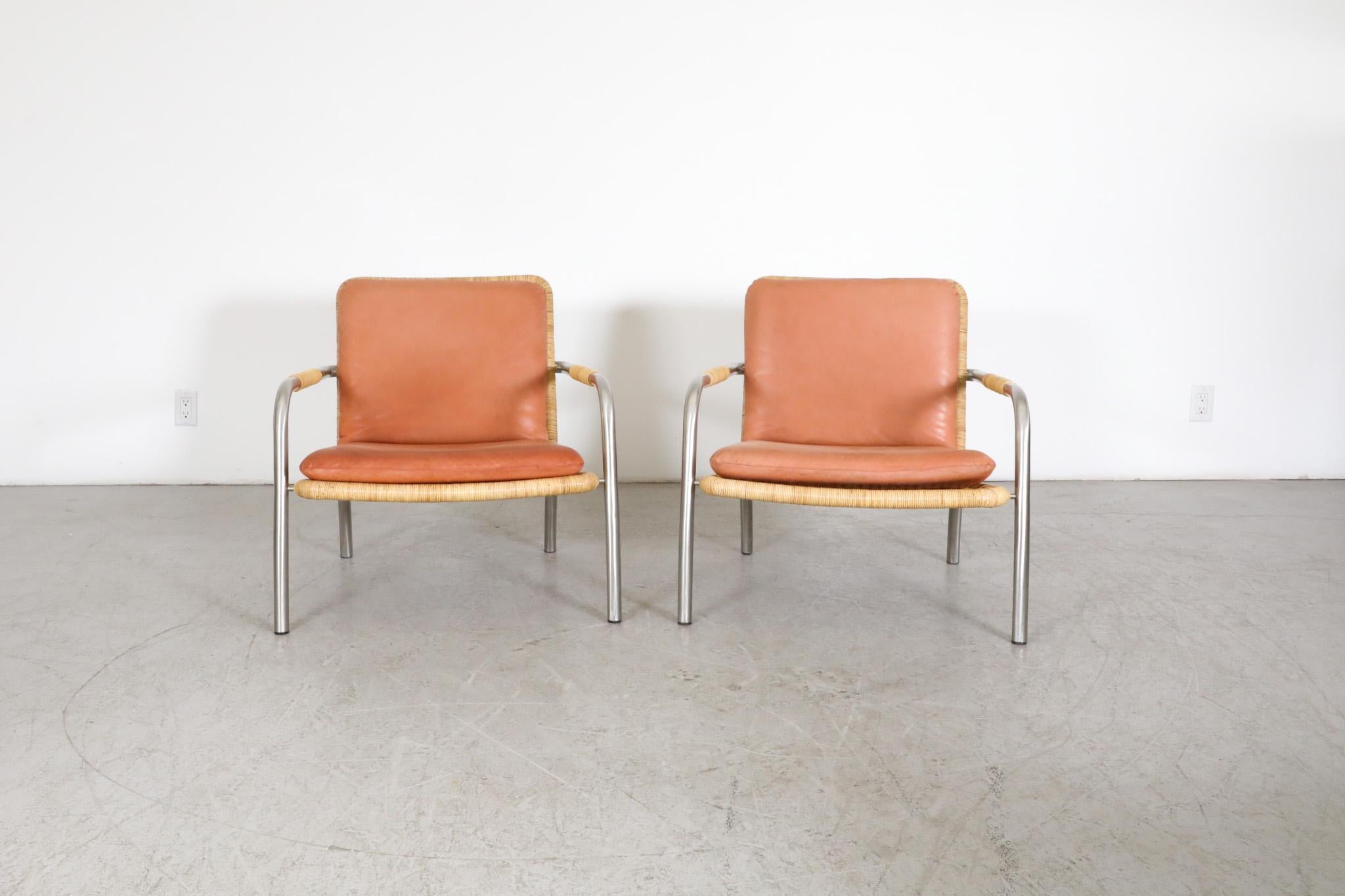 Stunning pair of Mid-Century, Martin Visser style woven rattan lounge chairs with lovely terracotta toned leather cushions on sturdy bent chrome frames. Handsome and comfortable lounge chairs with a beautiful balance of metal and leather and