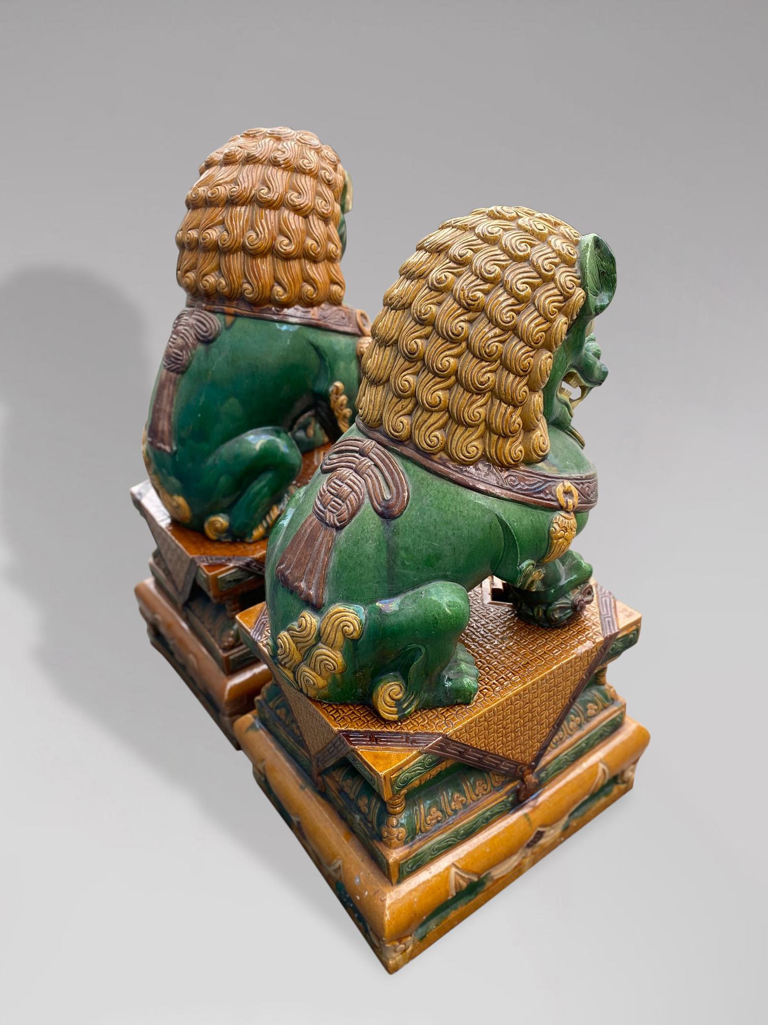 A large pair of unique and very decorative 20th century ceramic Imperial Guardian Lions, commonly known as Foo Dogs. Decorated in the Majolica style bright green and yellow toned overglaze polychrome ceramic. Both items in traditional dress and