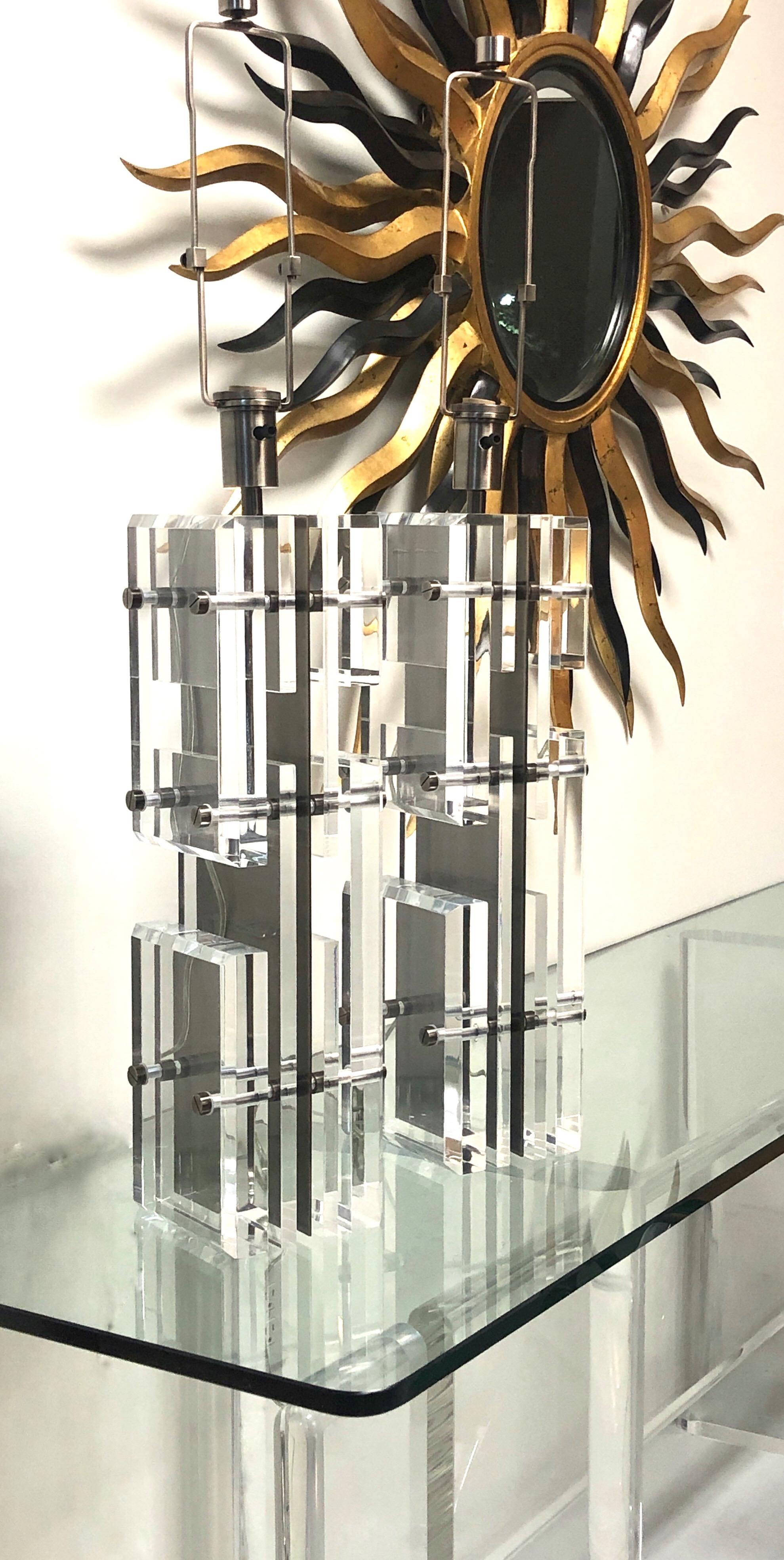 A pair of massive lamps. The body is comprised of multiple pieces of Lucite attached to a central metal piece by rods and custom screw finials. The Lucite pieces create an op art illusion with the brakes in the planes and the different sizes and