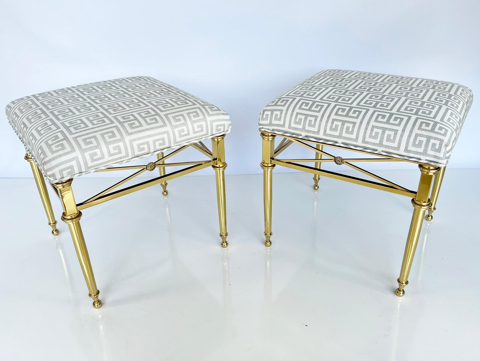 Pair of stools, each having a square upholstered crown seat, on frame of polished brass, raised on round, tapering legs, joined by box-stretcher, with cross decoration, centered with a rosette, ending in ball feet. 

Stock ID: D3354